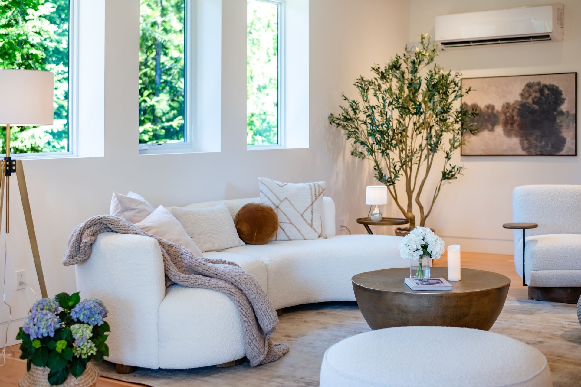 Bright living room with white sectional sofa, round coffee table, plants, and wall art