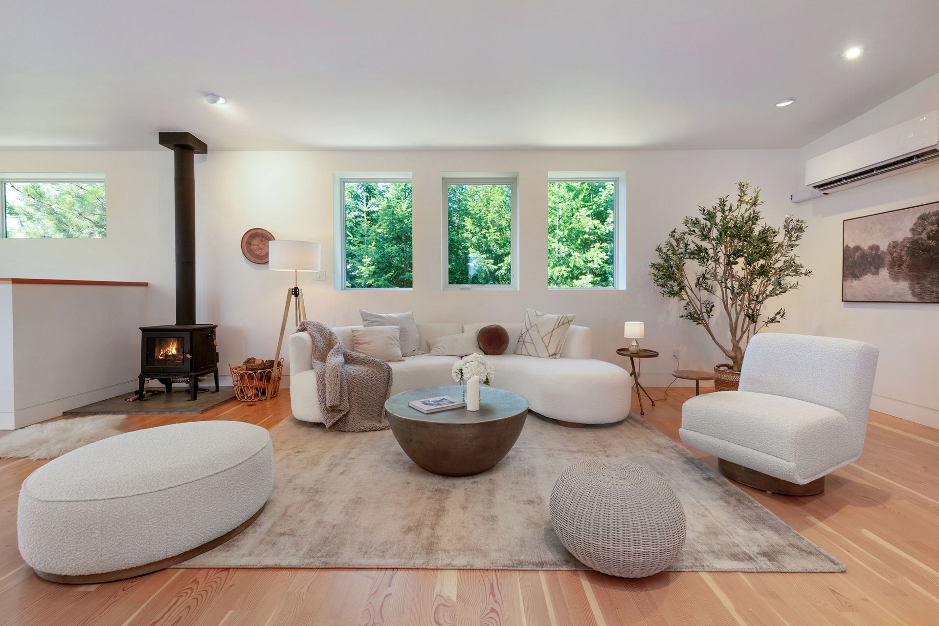 Bright minimalist living room with white chairs, round coffee table, wood floors, and large windows.