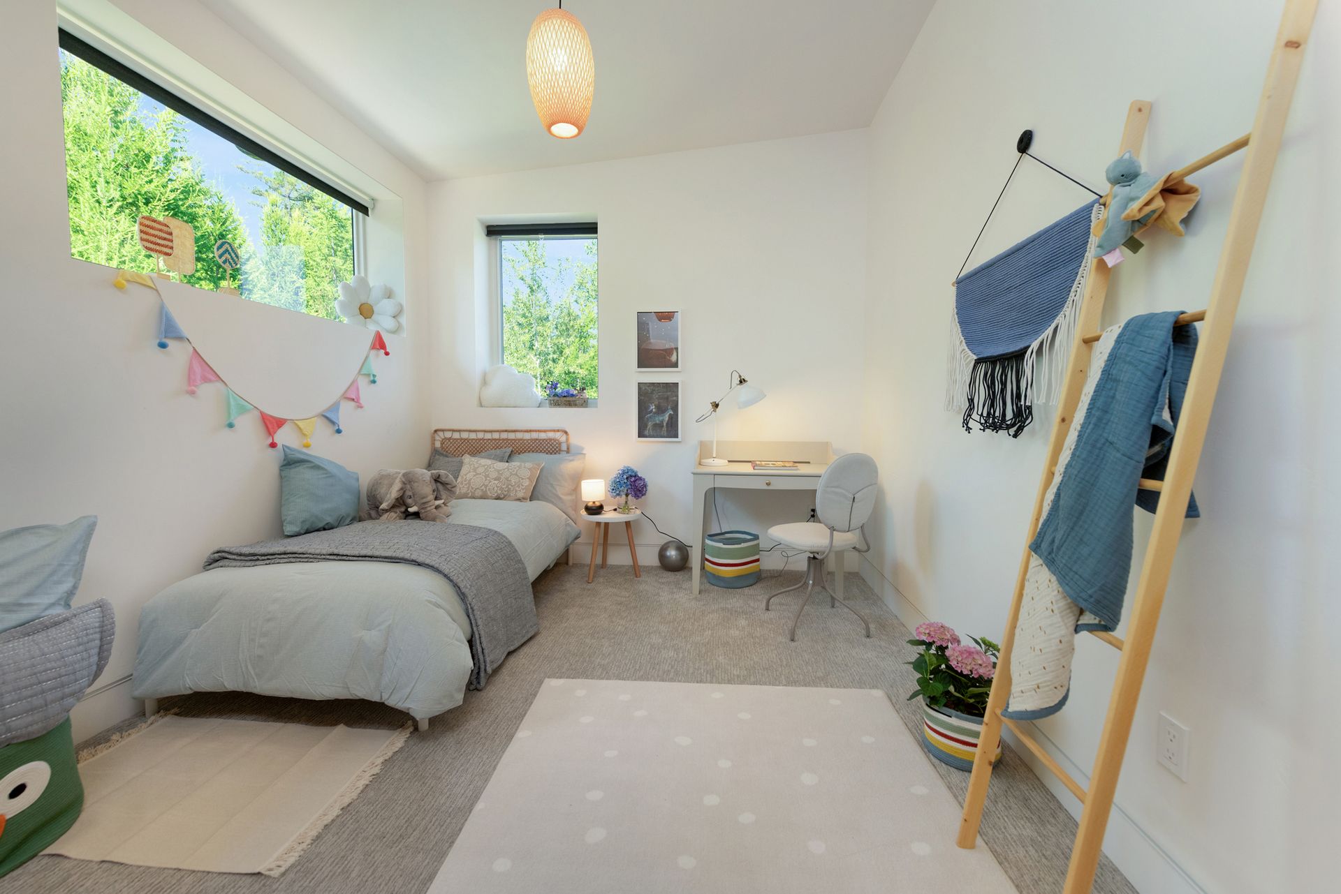 Bright cozy bedroom with bed, desk, ladder shelf, and bunting by large windows