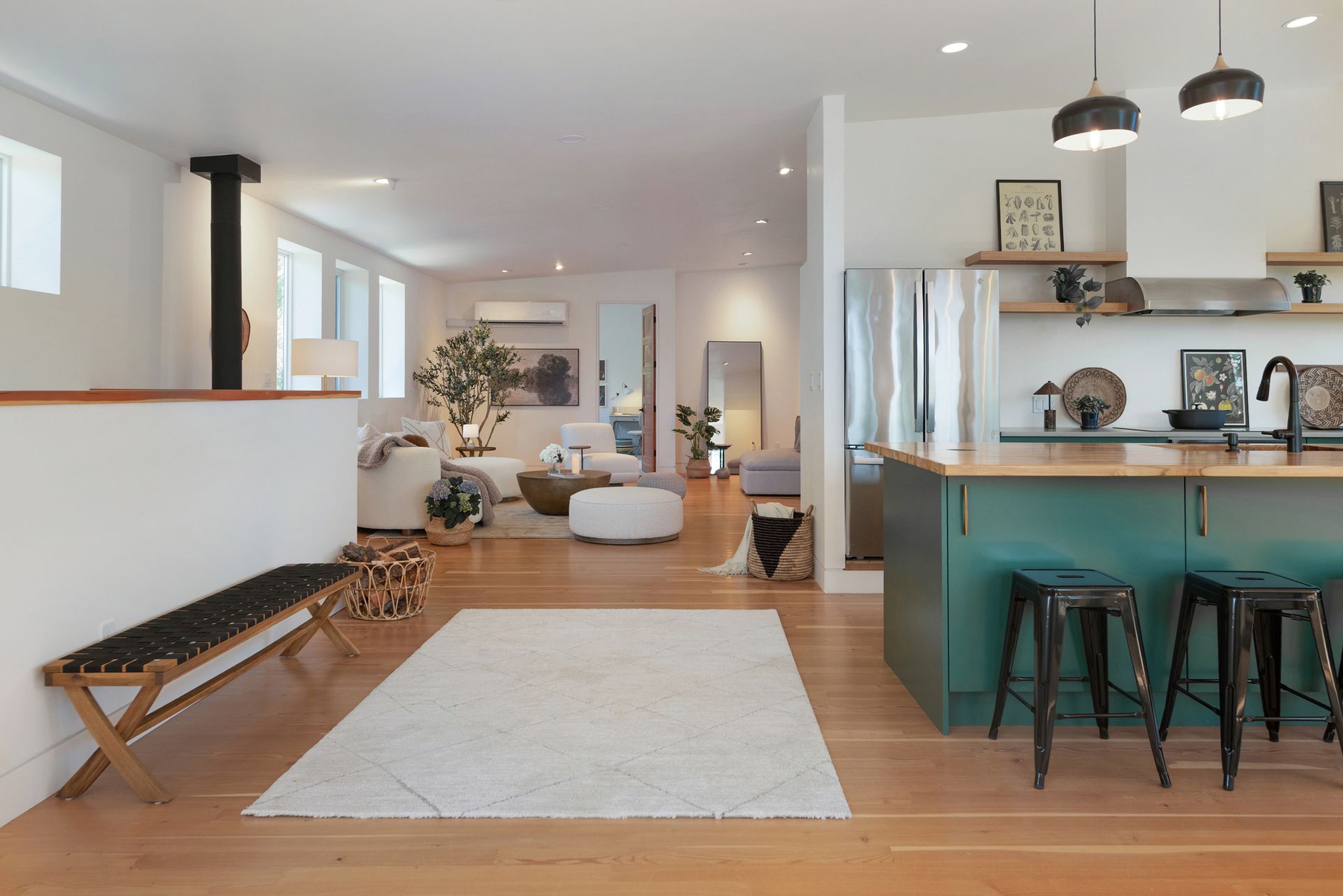 Open-plan living room with teal kitchen island, wood floors, white rug, and modern pendant lights