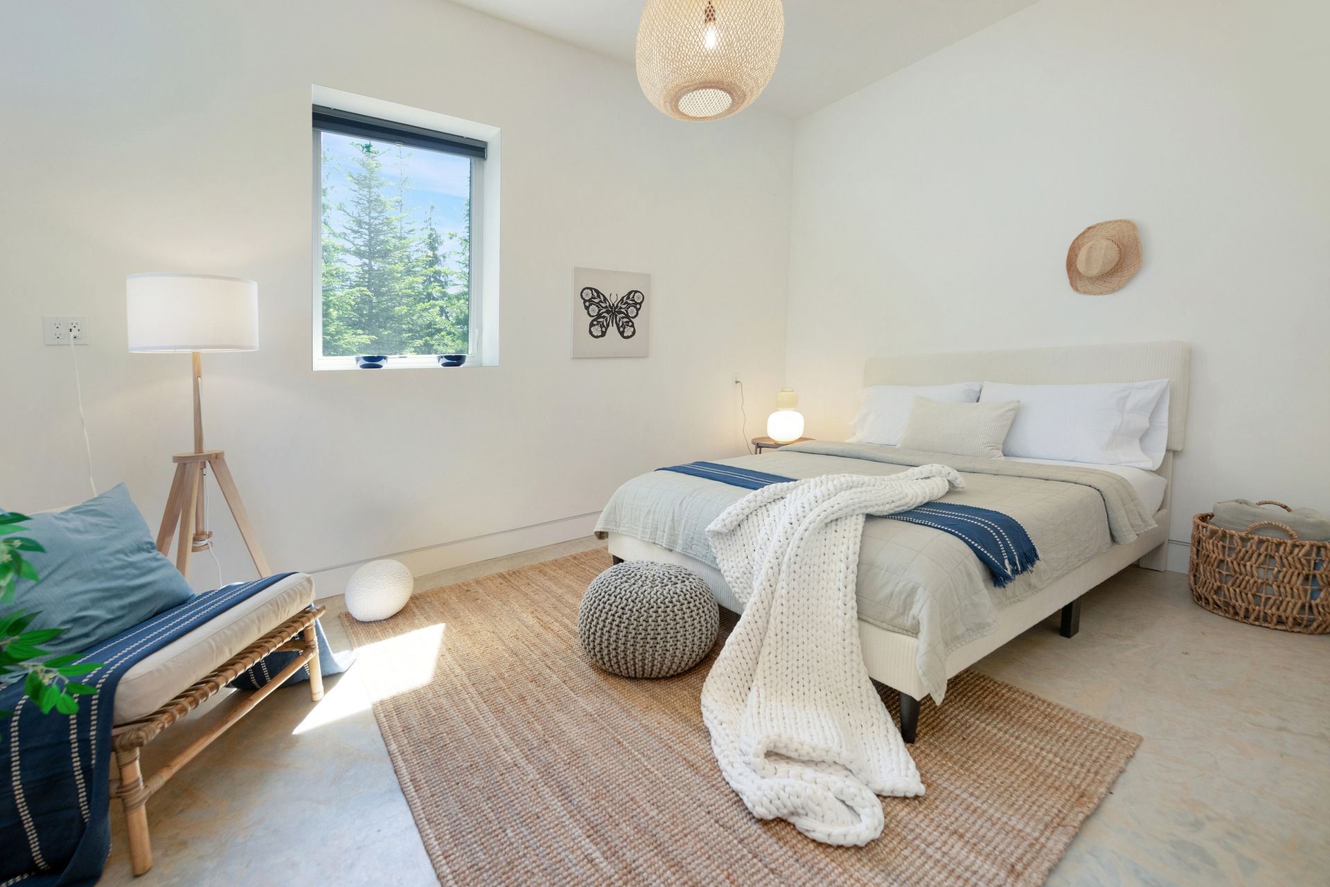 Bright bedroom with white bed, woven rug, blue bench, floor lamp, and sunlight through a window.