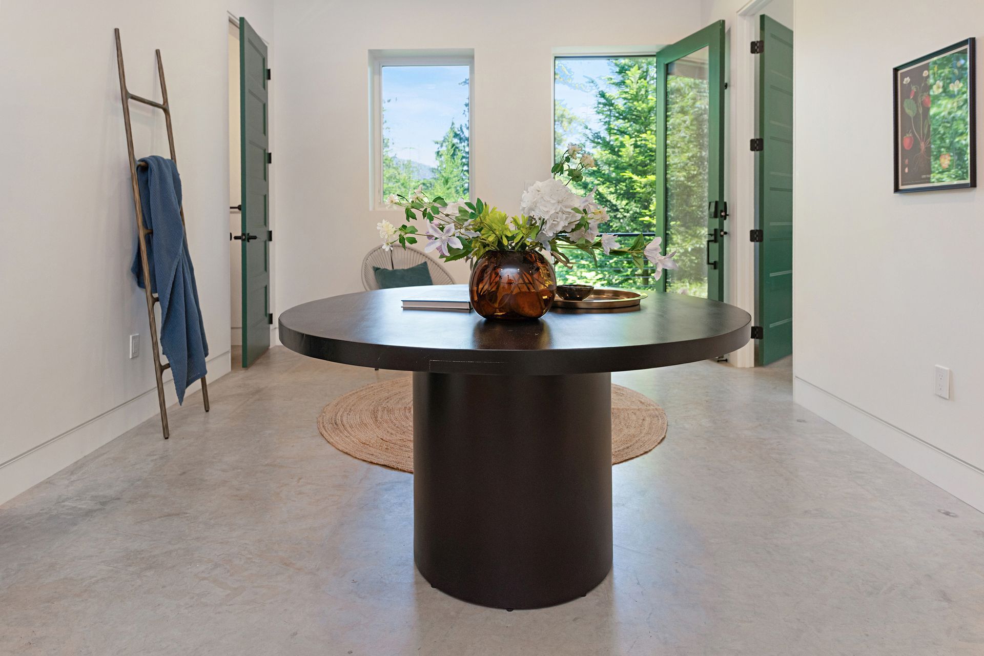 Bright modern room with open doors, a round black table, and a plant centerpiece on a woven rug.