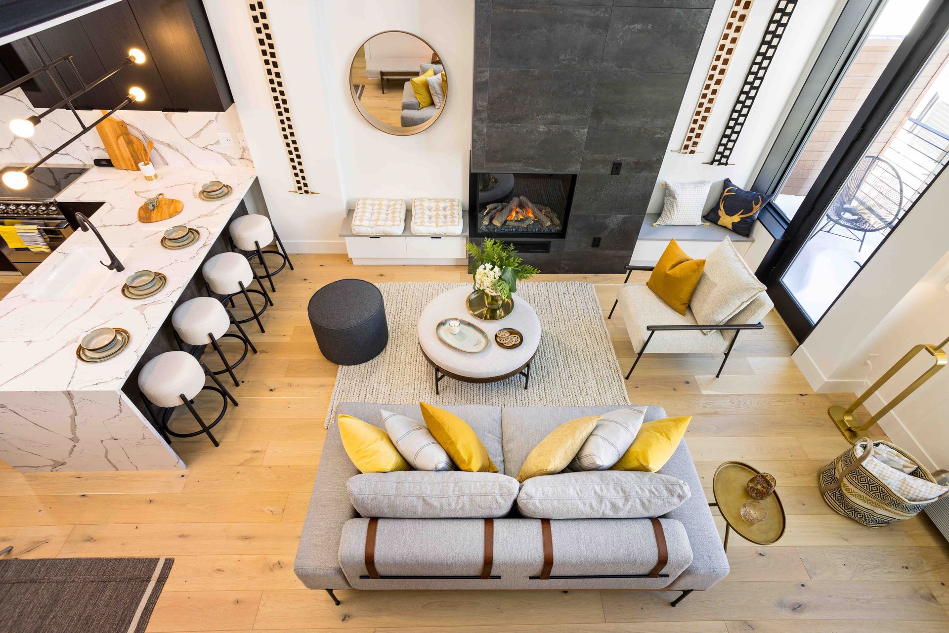 Open-plan living room with gray sofa, yellow pillows, round coffee table, and kitchen bar stools.