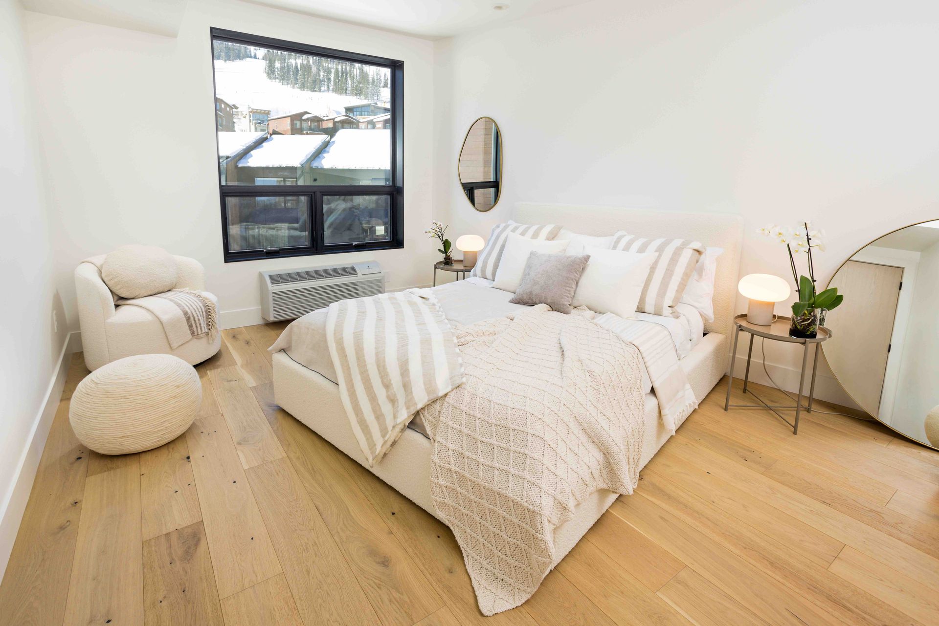 Bright bedroom with white bedding, wood floors, large window, and a small bedside lamp