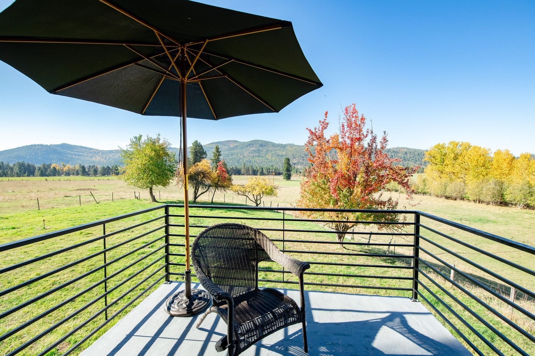 Patio deck with black chair and umbrella overlooking a sunny field and autumn trees