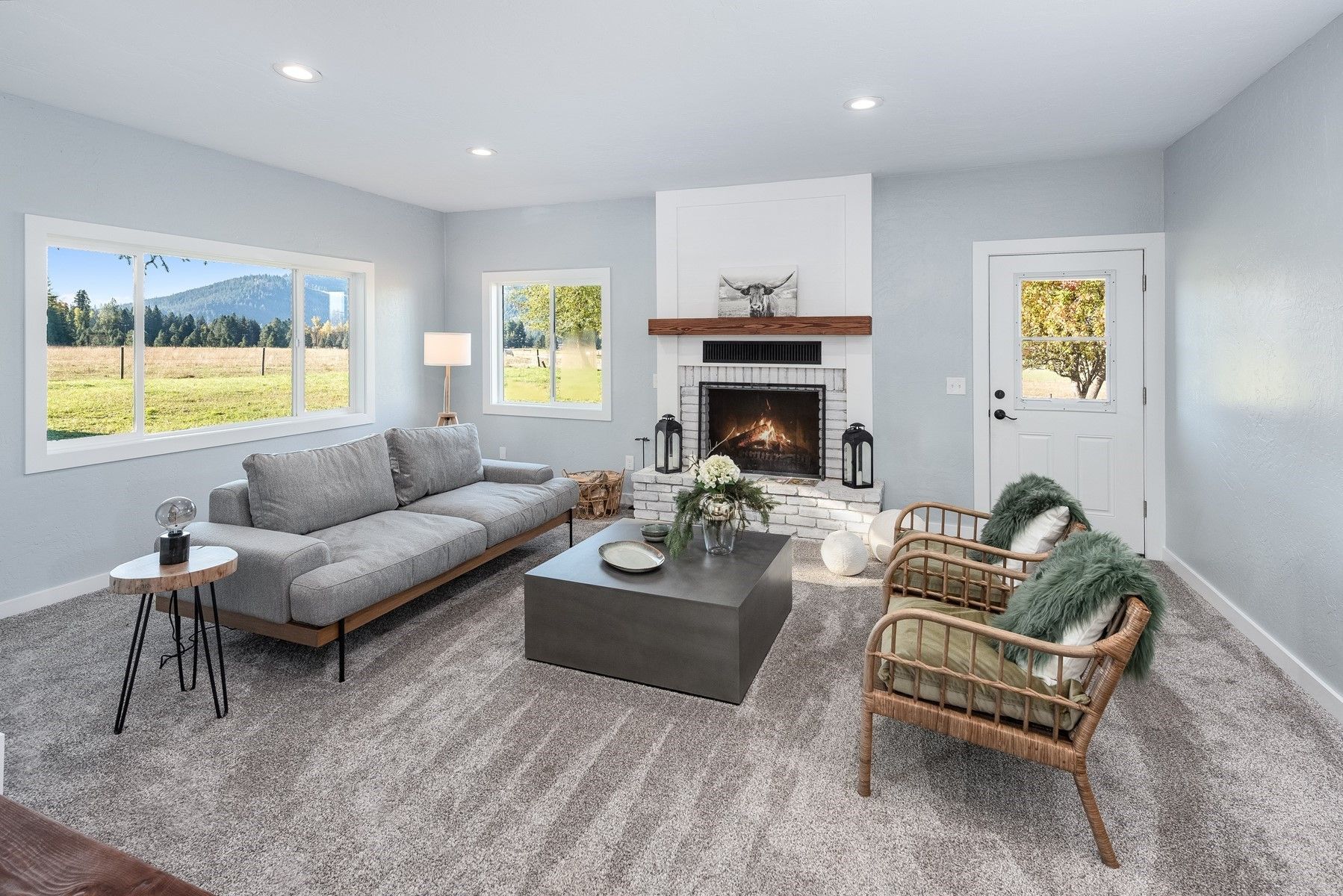 Bright living room with gray sofa, green chair, coffee table, and fireplace beside large windows.
