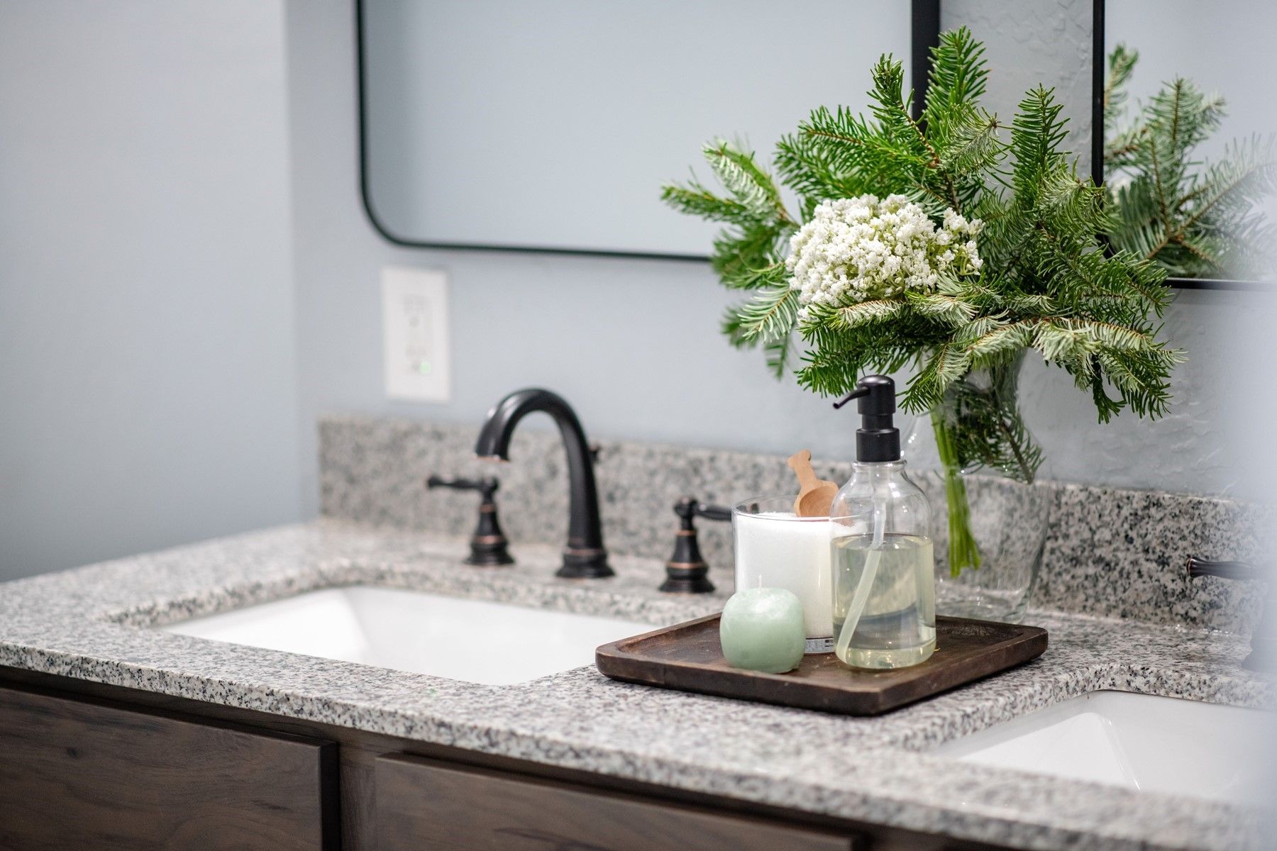 Bathroom vanity with black faucet, speckled countertop, lit candle, and white flowers in a vase