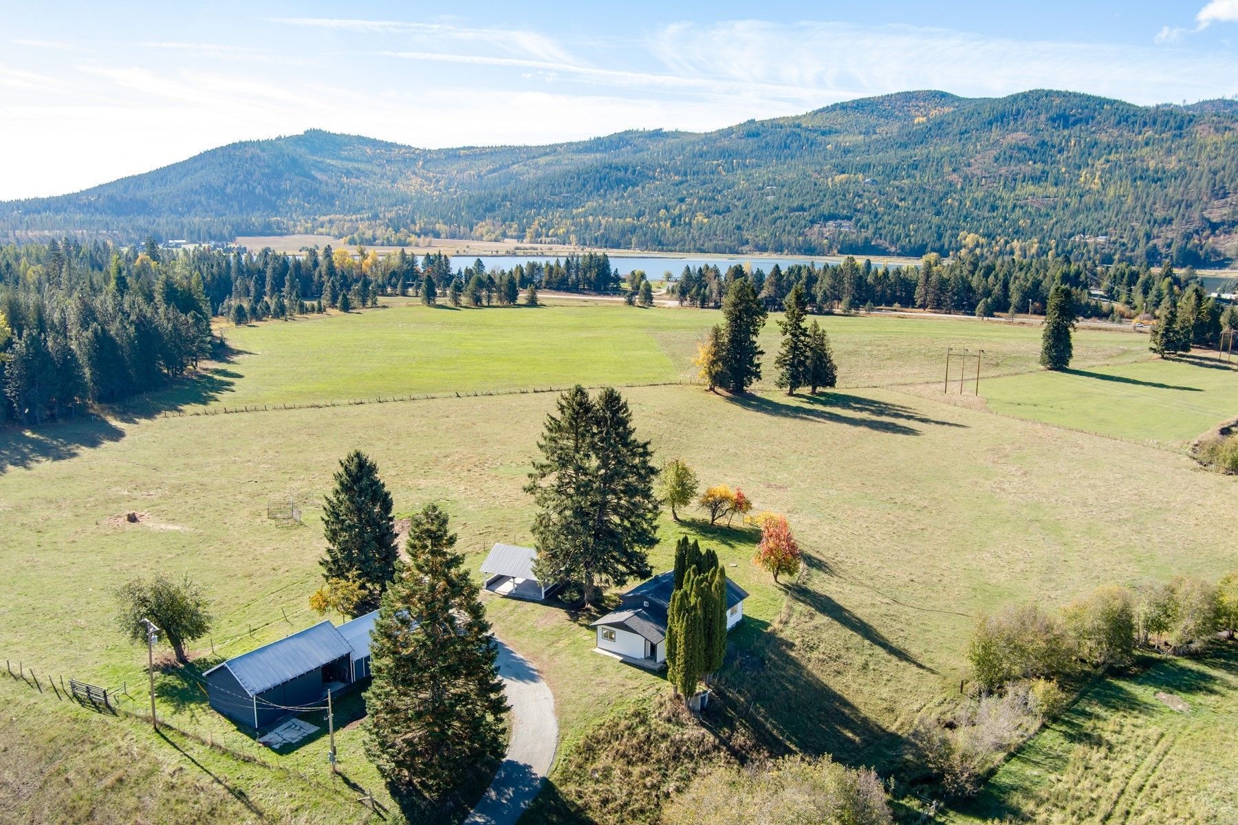 Aerial view of a rural valley with green fields, scattered trees, a farmhouse, and forested hills under a clear sky