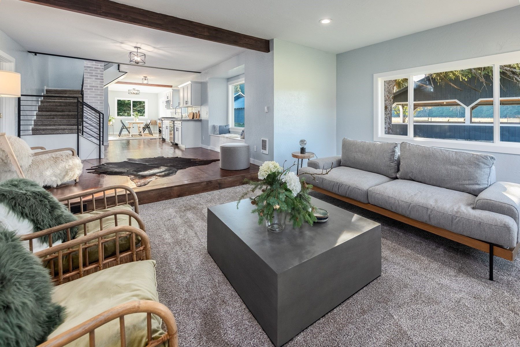 Bright modern living room with gray sofa, woven chairs, coffee table, and ocean-view windows