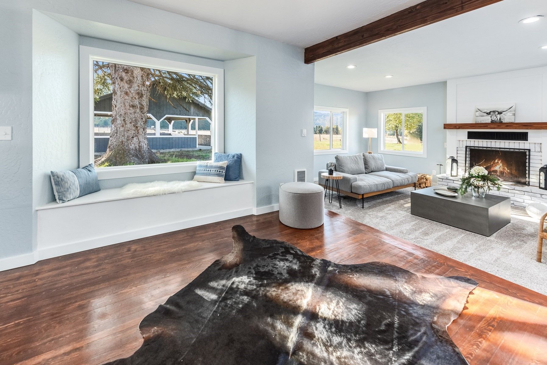 Bright living room with a large window seat, hardwood floors, fireplace, and cowhide rug