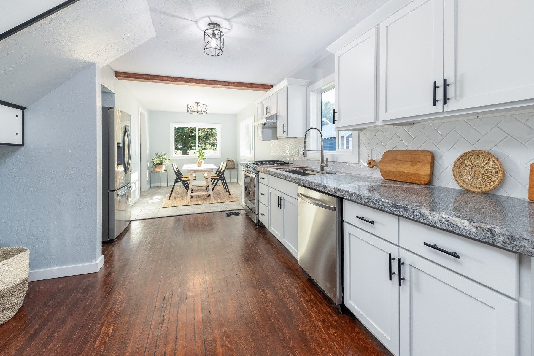 Bright white kitchen with granite counters, dark wood floors, and a dining area beyond the doorway