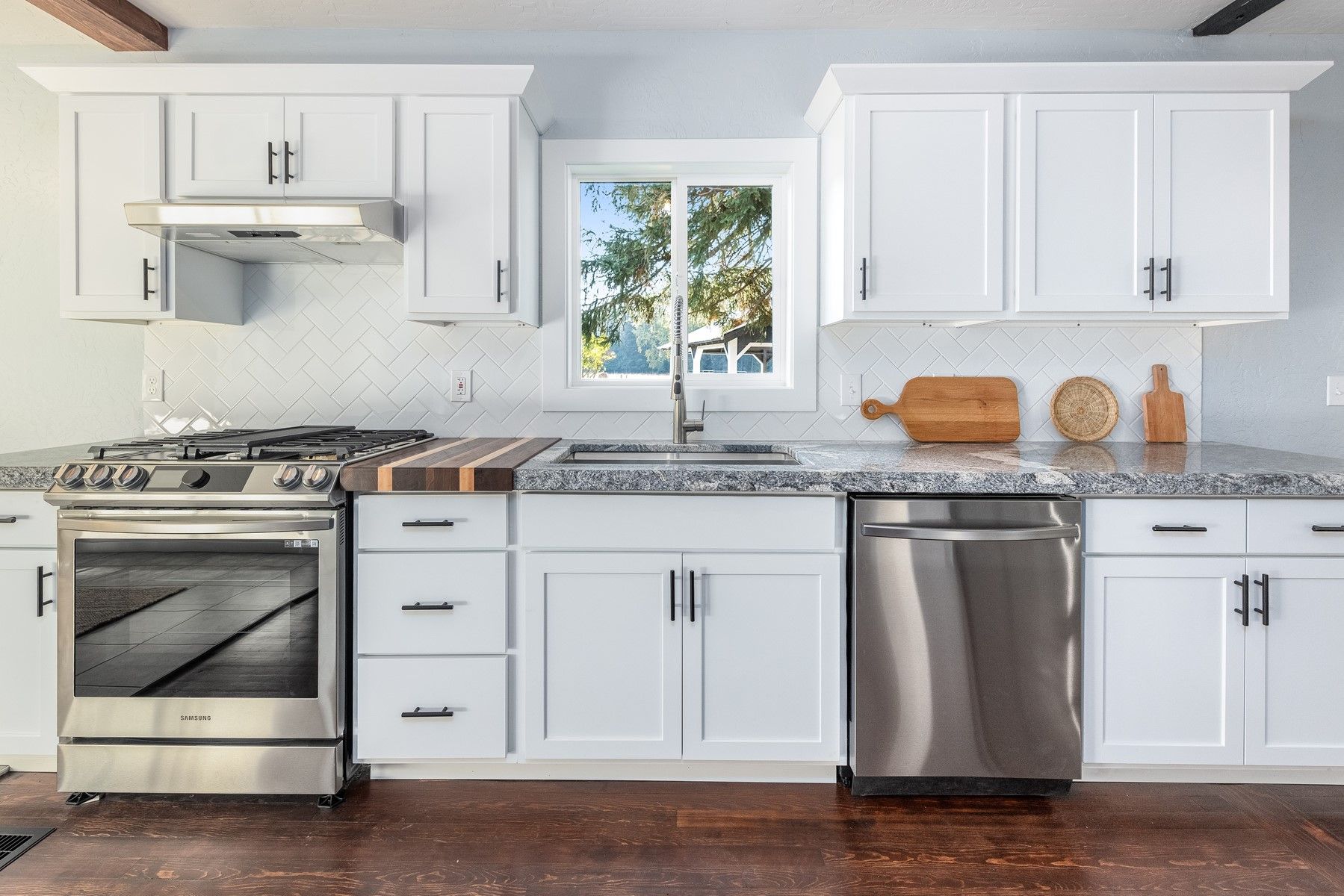 Modern white kitchen with stainless steel appliances and a central window over the sink