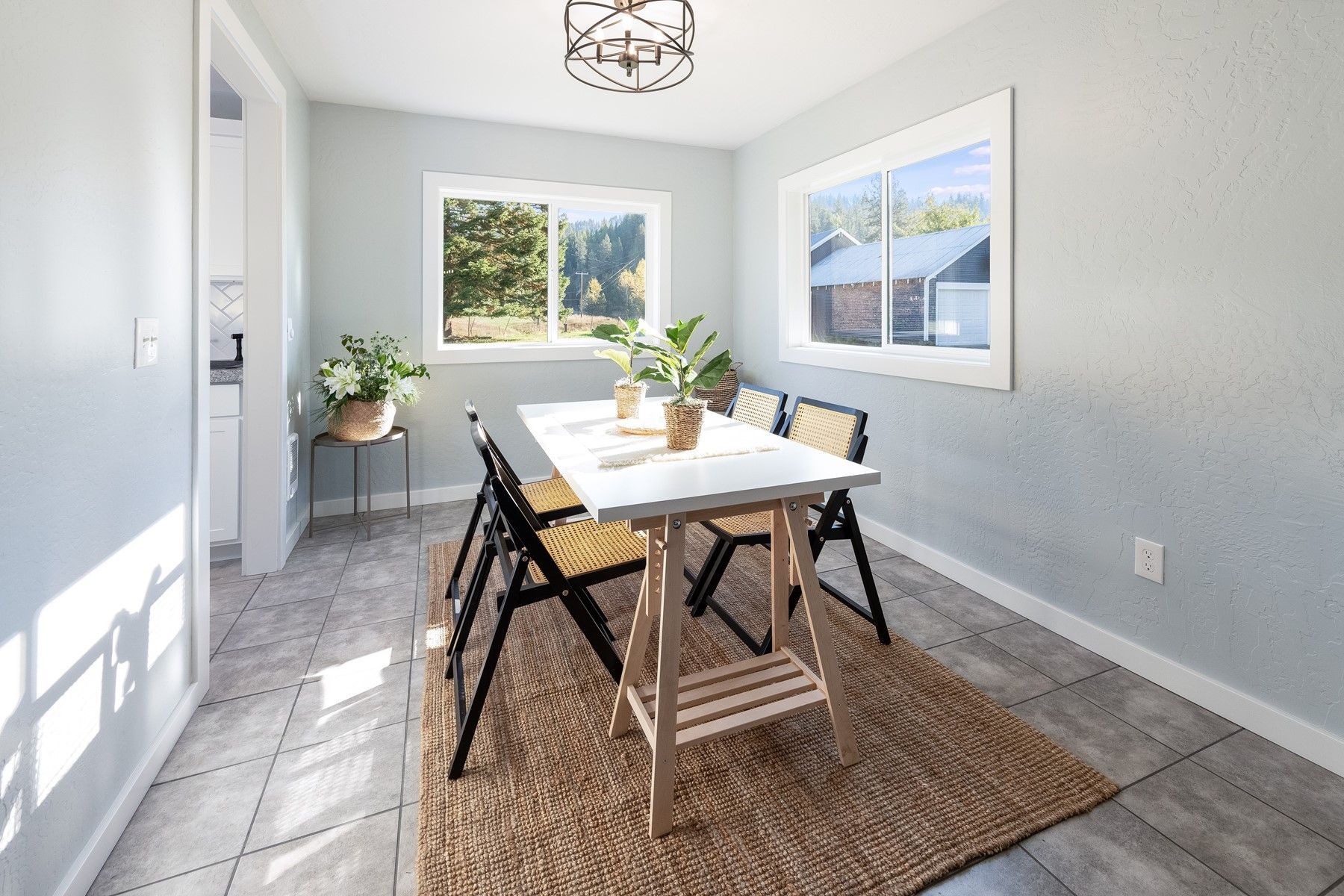 Bright dining nook with white walls, a table, black chairs, a jute rug, and sunlight from two windows.