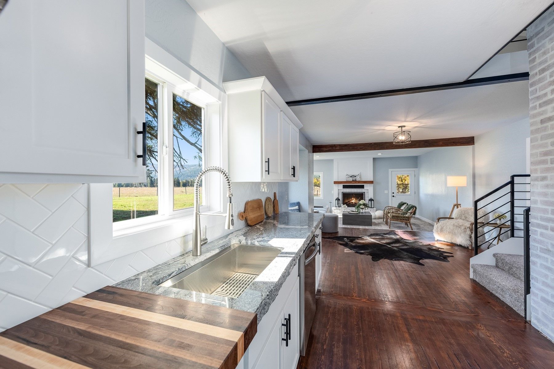 Bright modern kitchen opening to a living room with white cabinets, wood floors, and large windows