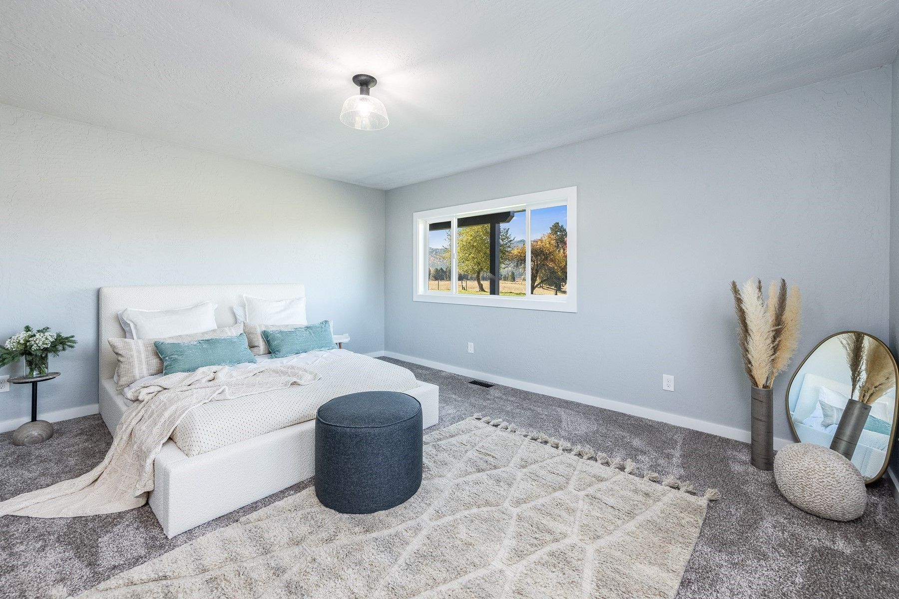Bright bedroom with white bed, gray rug, window, and decorative mirror and vases