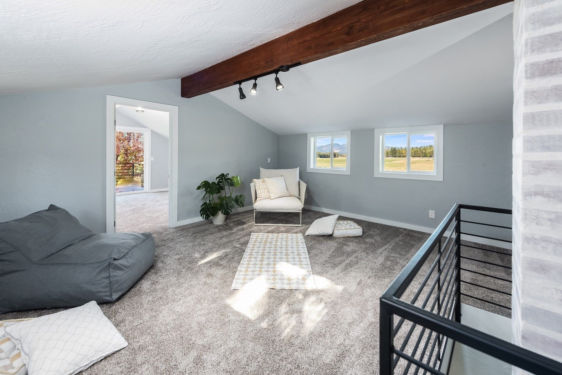 Bright loft living room with gray carpet, dark beams, beanbag chair, and black stair railing