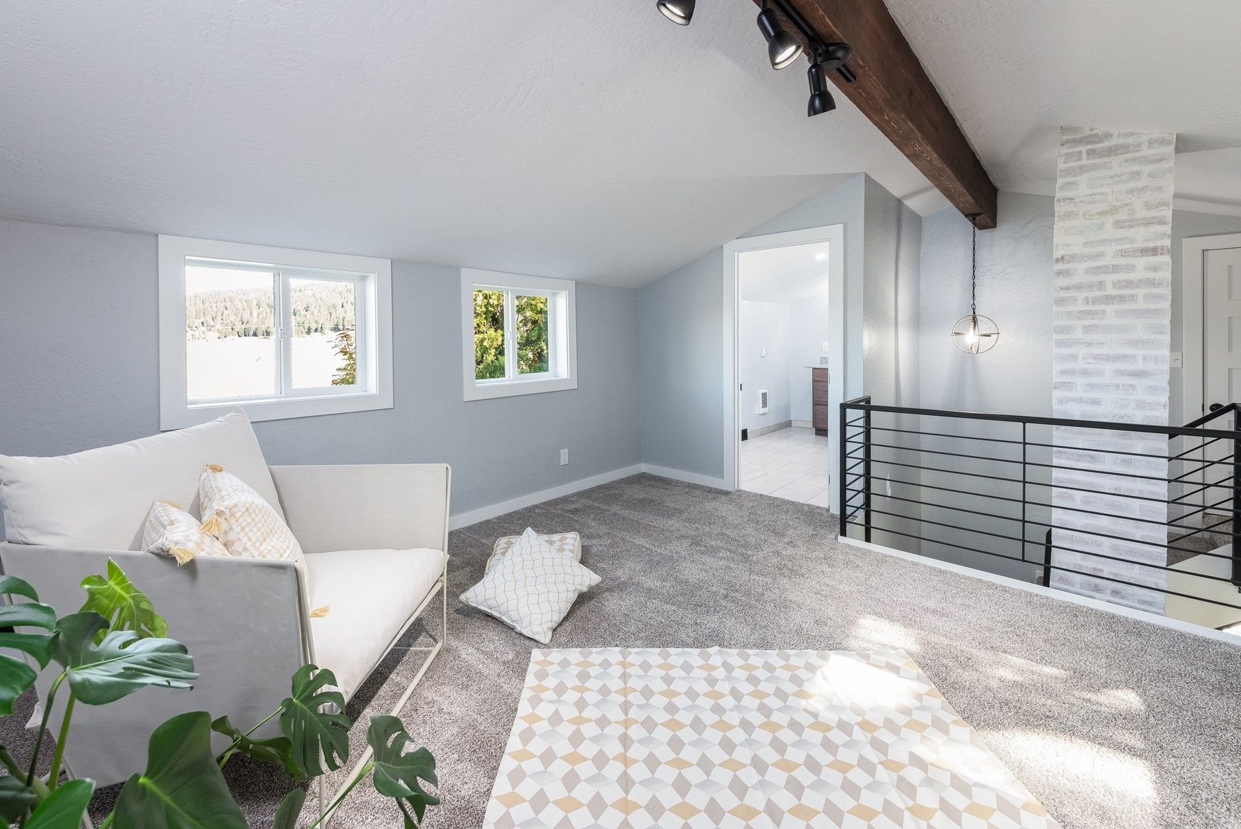 Bright attic bedroom with windows, white sofa, patterned rug, and black railing by a staircase.