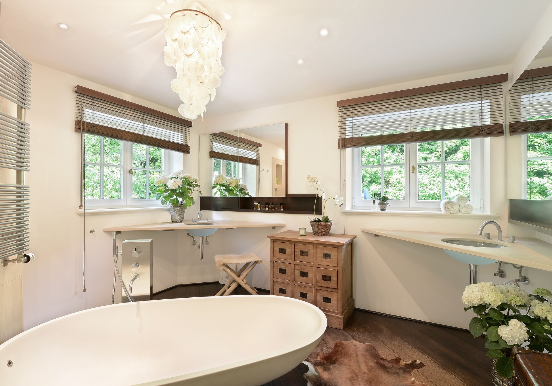 Bright bathroom with a freestanding tub, large windows, a vanity, and a floral chandelier.