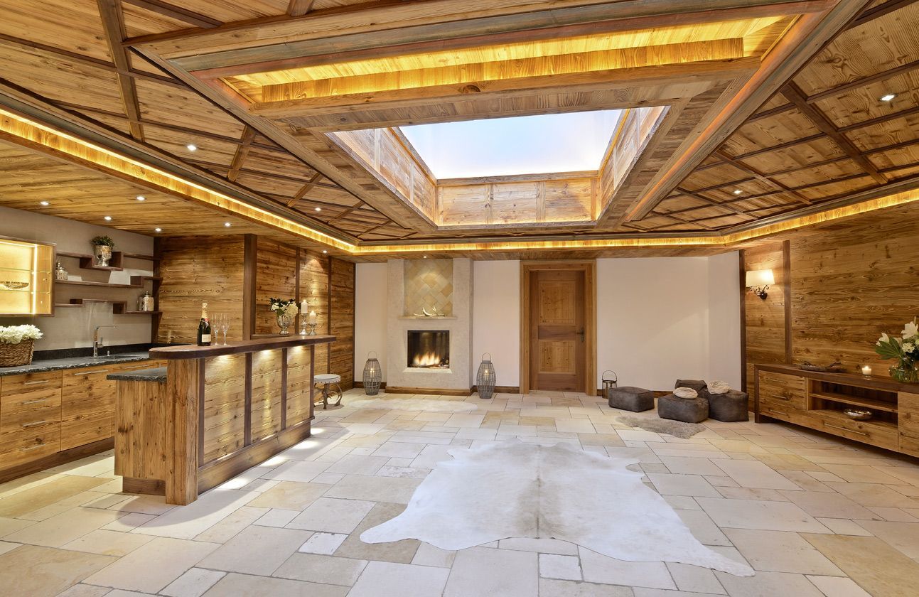 Empty rustic wood-paneled room with a skylight, exposed beams, fireplace, and a bar area on the left.