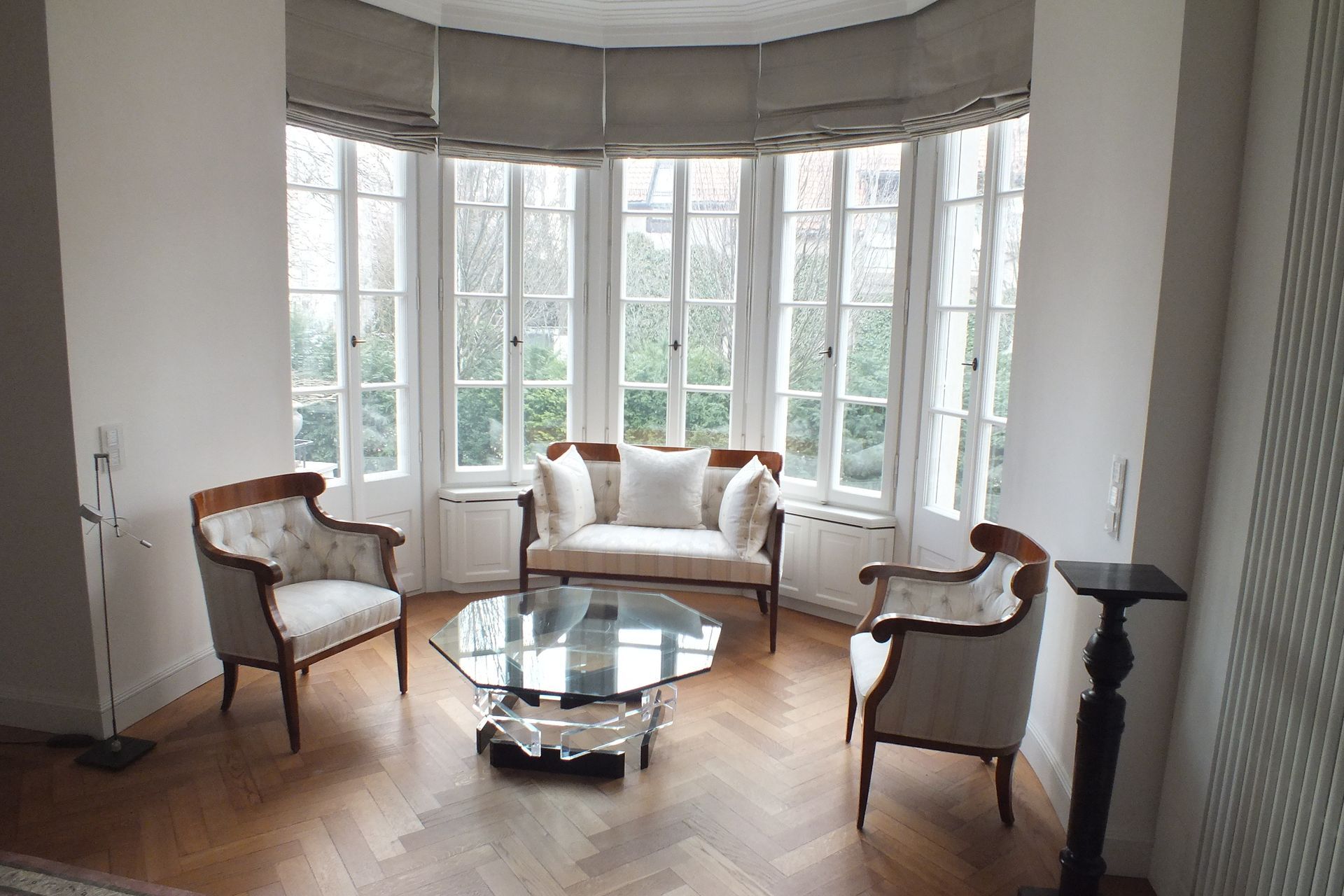 Bright sitting room with bay windows, white upholstered chairs, and a glass coffee table on wood floors