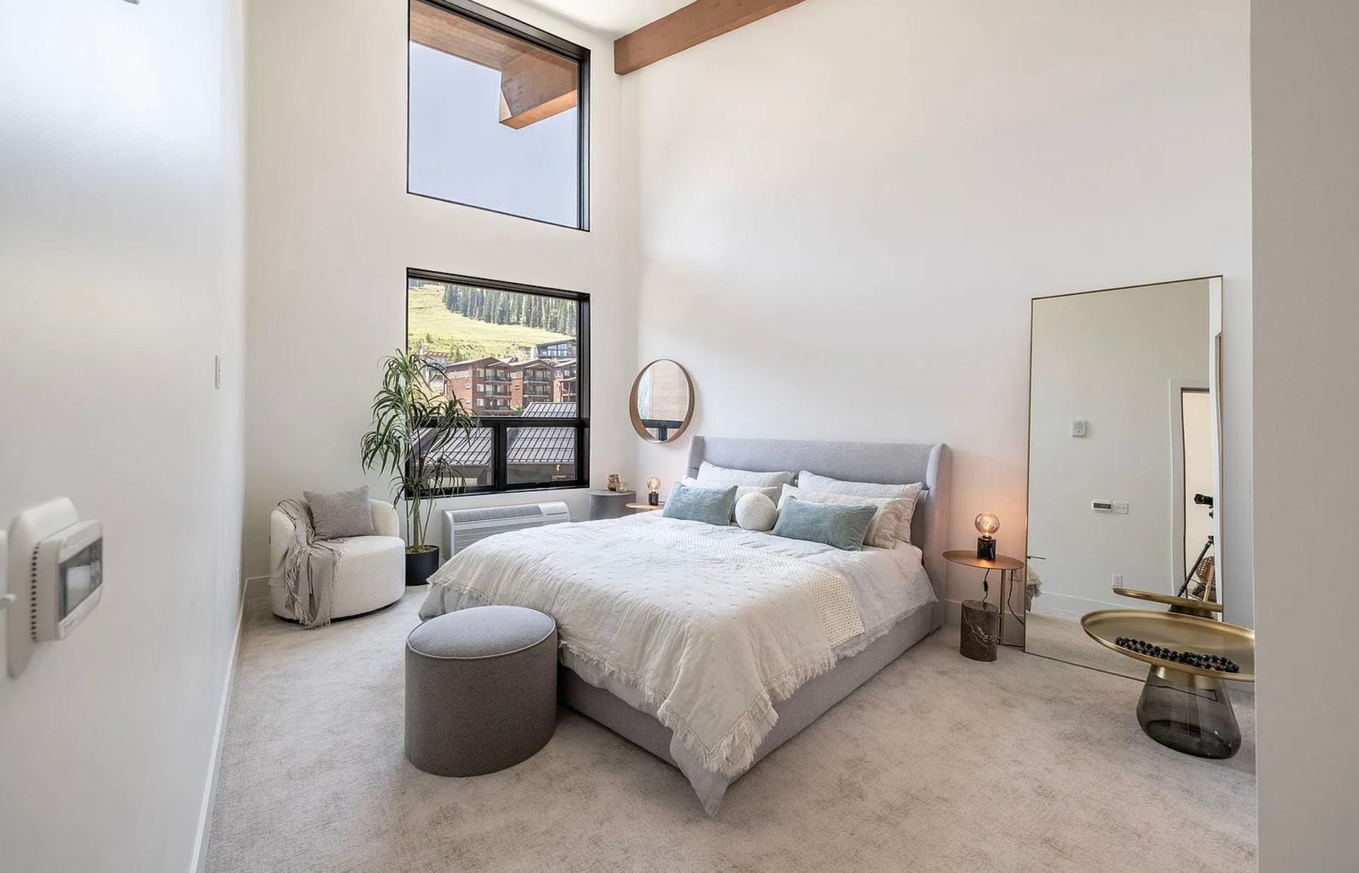 Bright bedroom with white bed, tall mirror, potted plant, and soft natural light