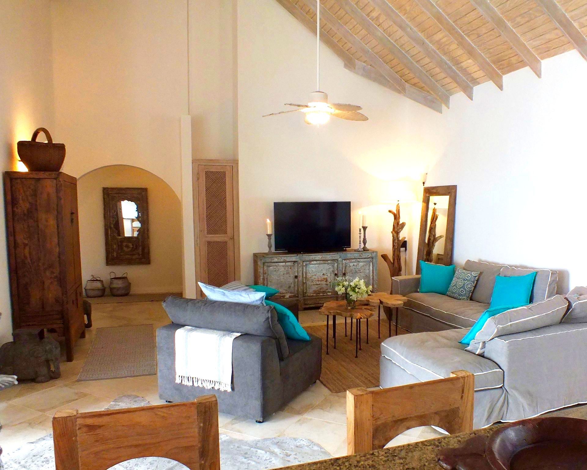 Cozy living room with high wood ceiling, fireplace, TV, and gray sofas accented with turquoise pillows