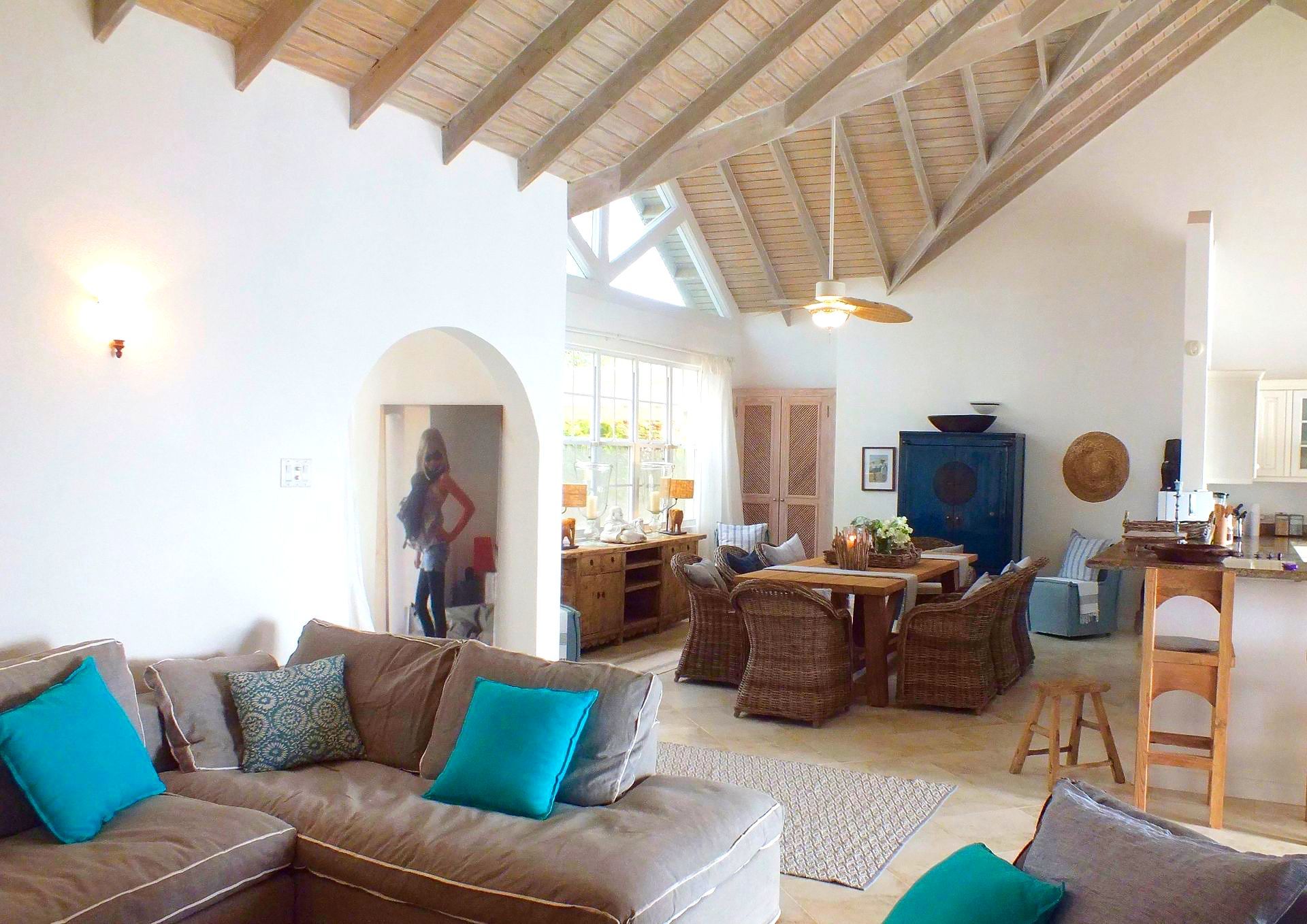 Bright living room with vaulted wood ceiling, brown sofa, wicker dining set, and turquoise pillows