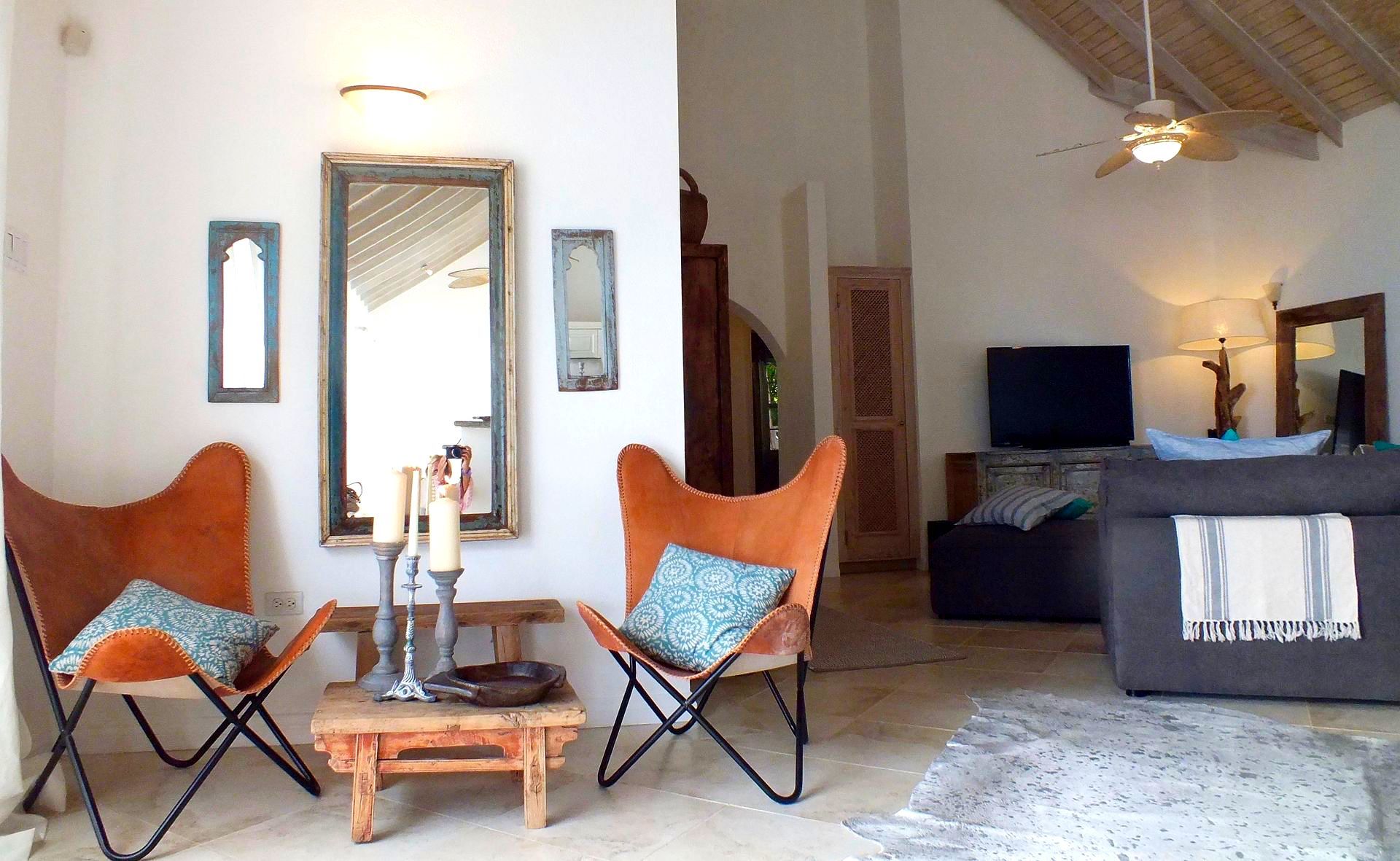 Cozy living room with two orange chairs, a small table, wall mirrors, and a sofa facing a TV.