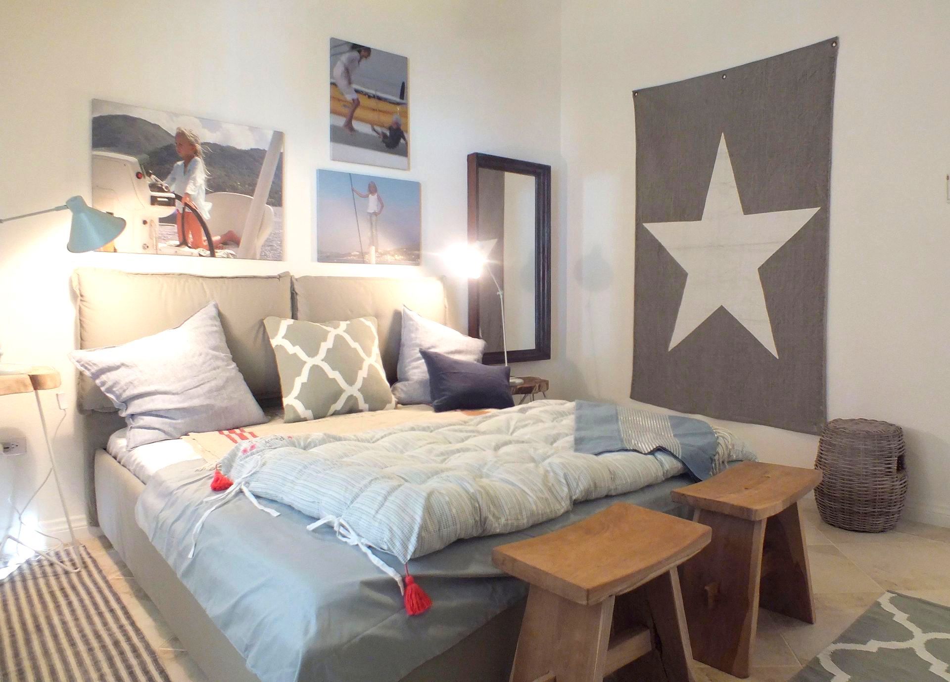 Cozy bedroom with unmade bed, gray and white decor, star wall art, and bedside lamps illuminated.
