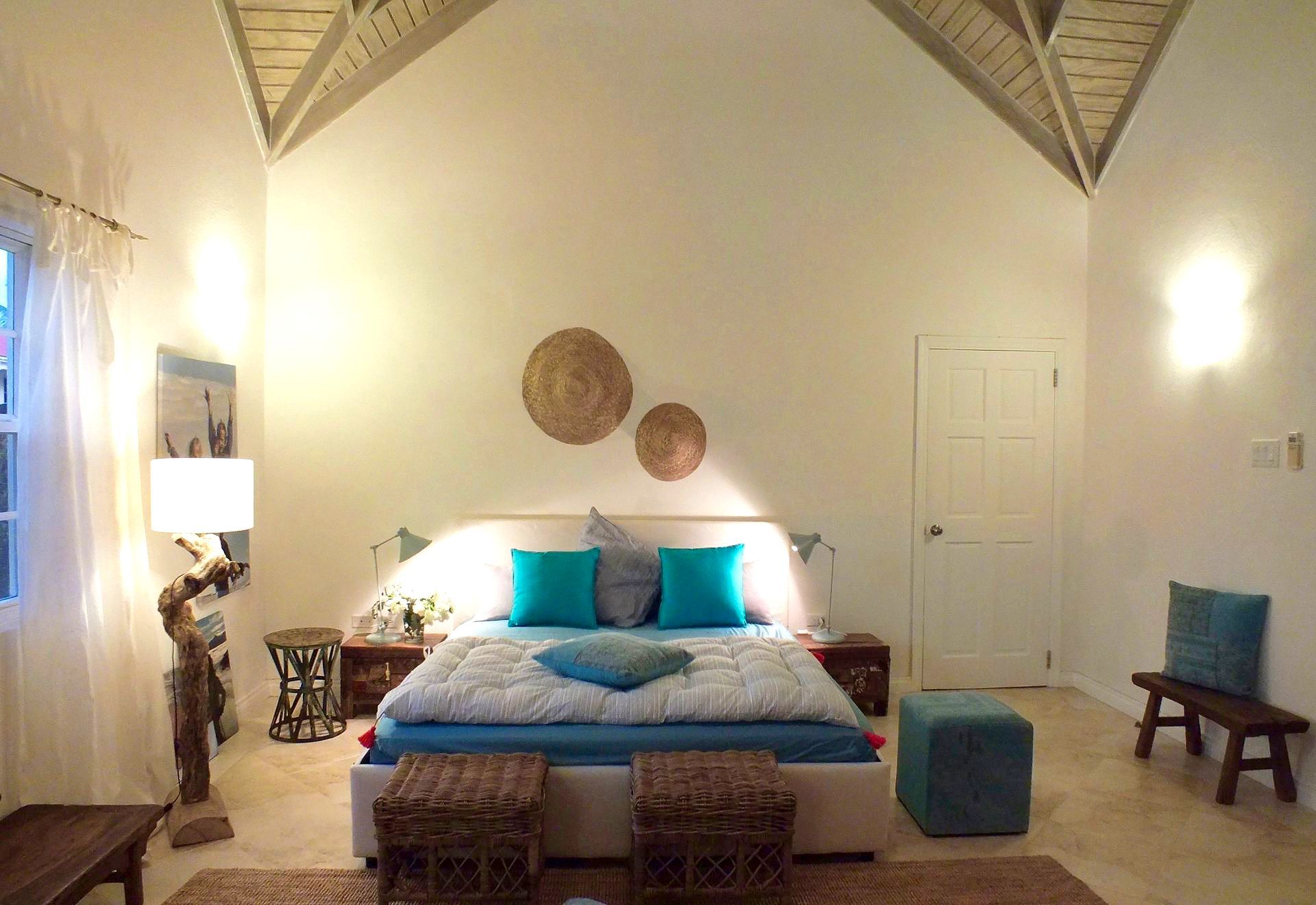 Cozy bedroom with a bed, teal pillows, woven decor, and warm wall lighting under a vaulted ceiling