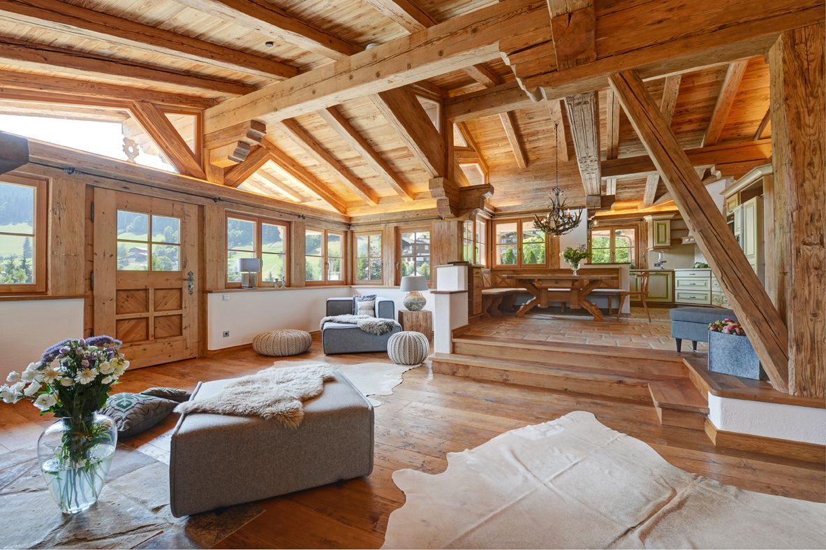 Rustic open-plan cabin interior with exposed beams, wood floors, large windows, and modern furniture