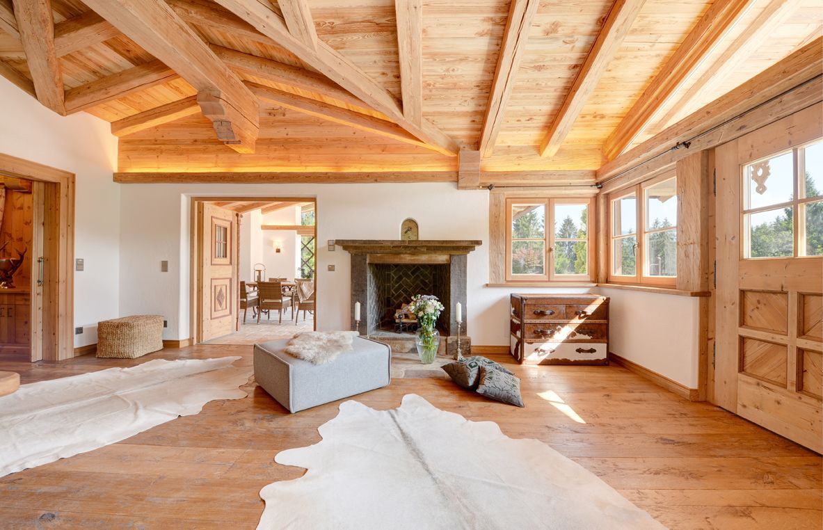 Spacious rustic living room with exposed beams, stone fireplace, wood floors, and large windows