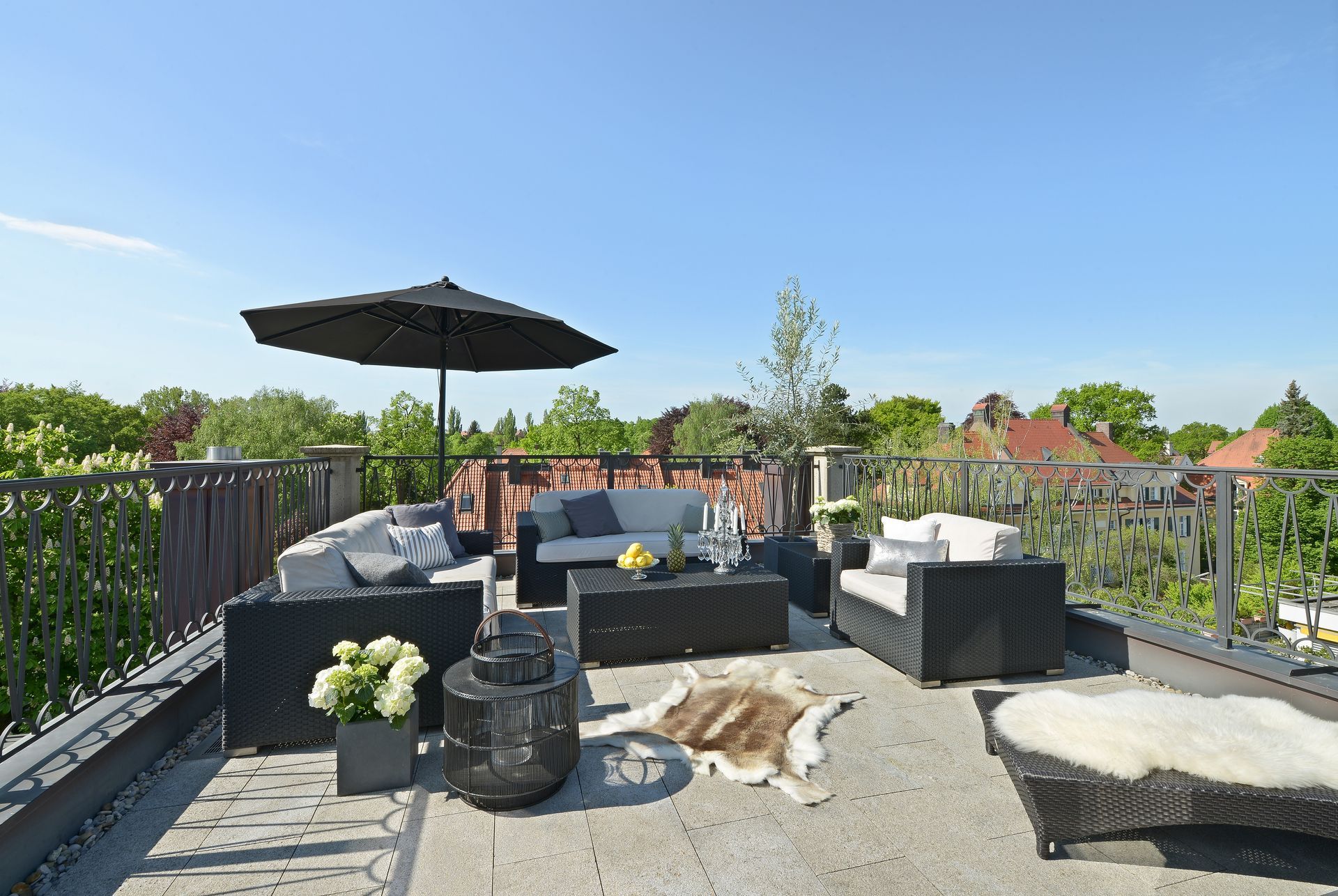 Patio lounge with black wicker seating, umbrella, and stone fire pit under a clear blue sky