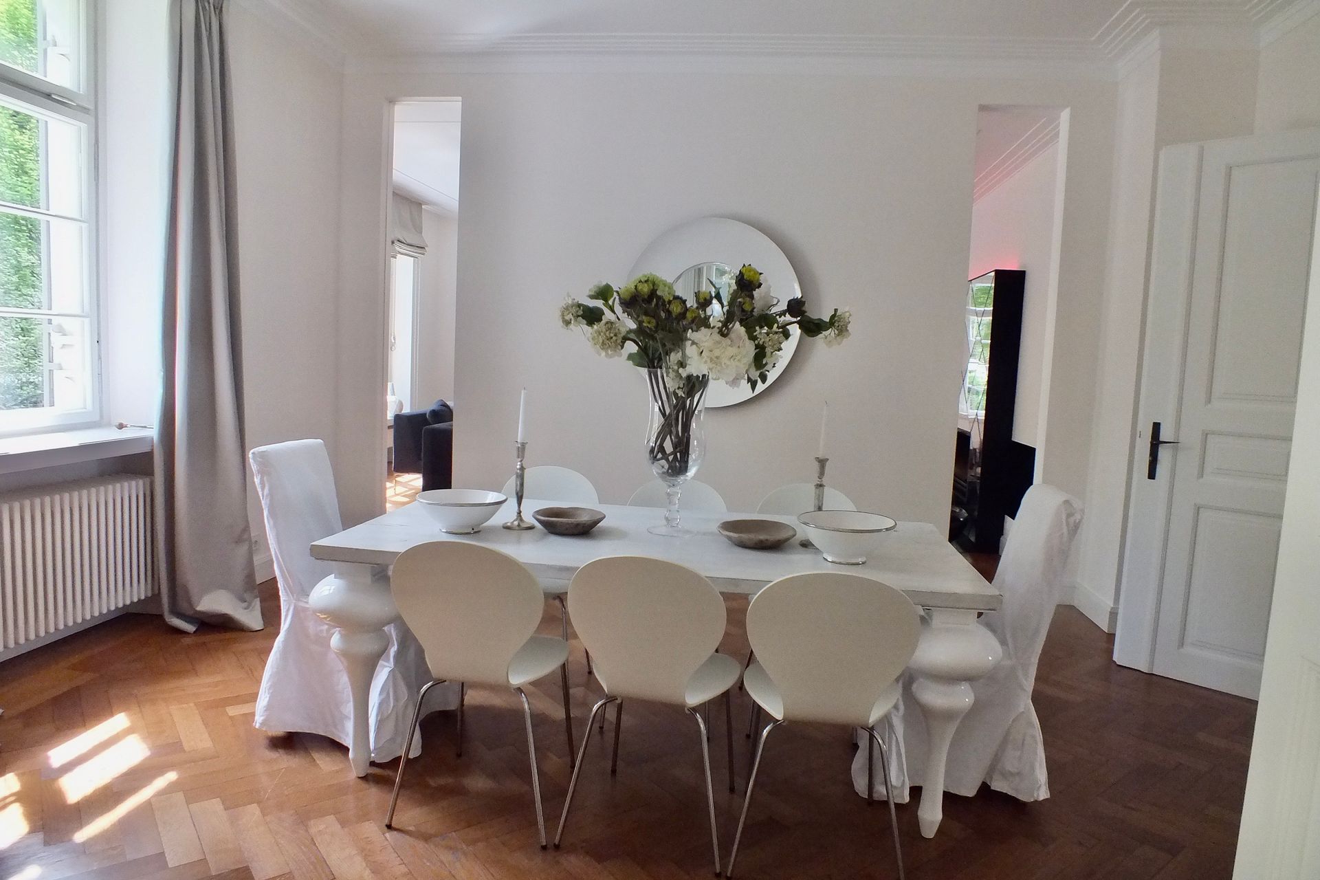 Dining room with a white table, chairs, and a vase of flowers by a bright window.