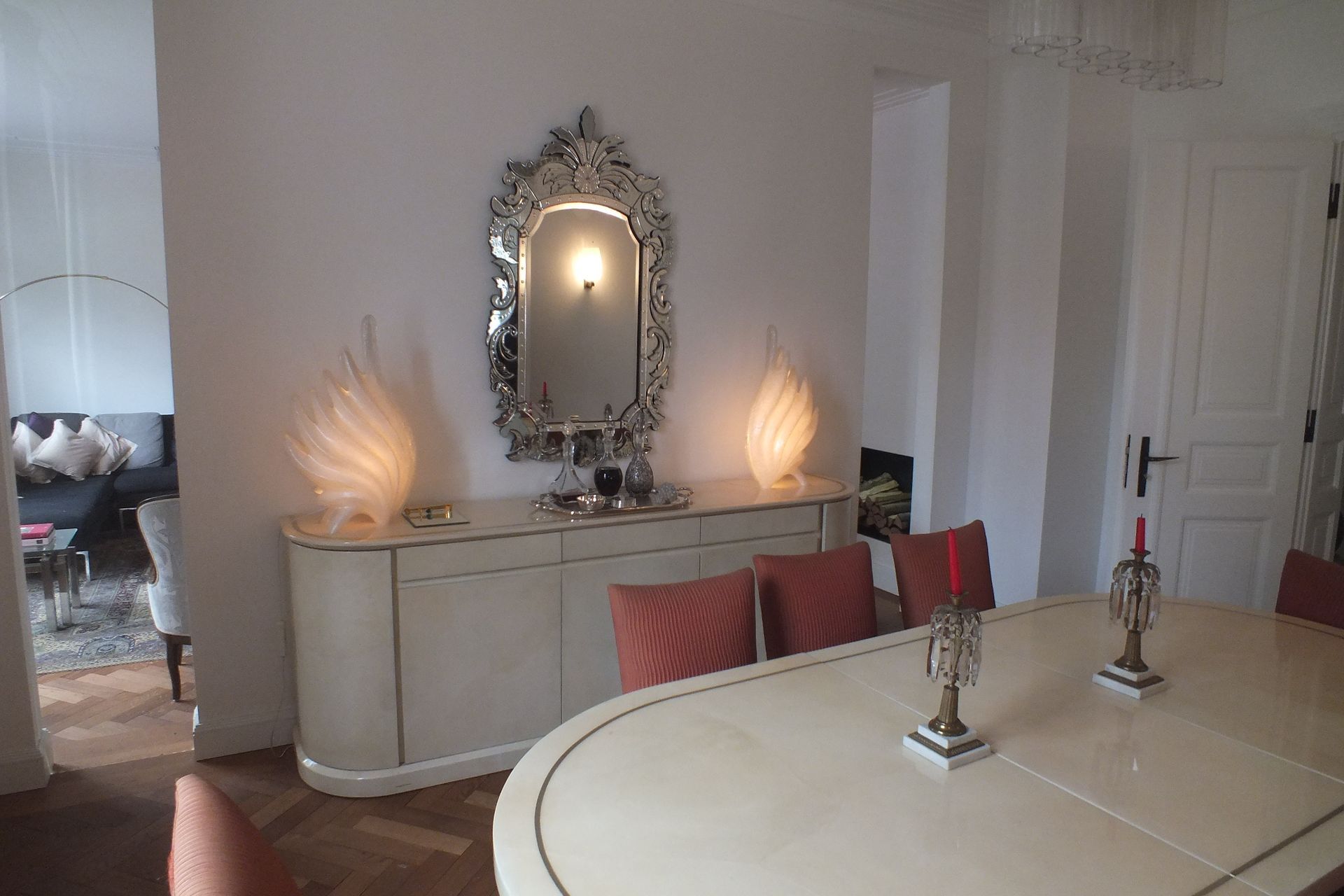 Elegant dining room with ornate console, mirror, wall sconces, and a round table in the foreground