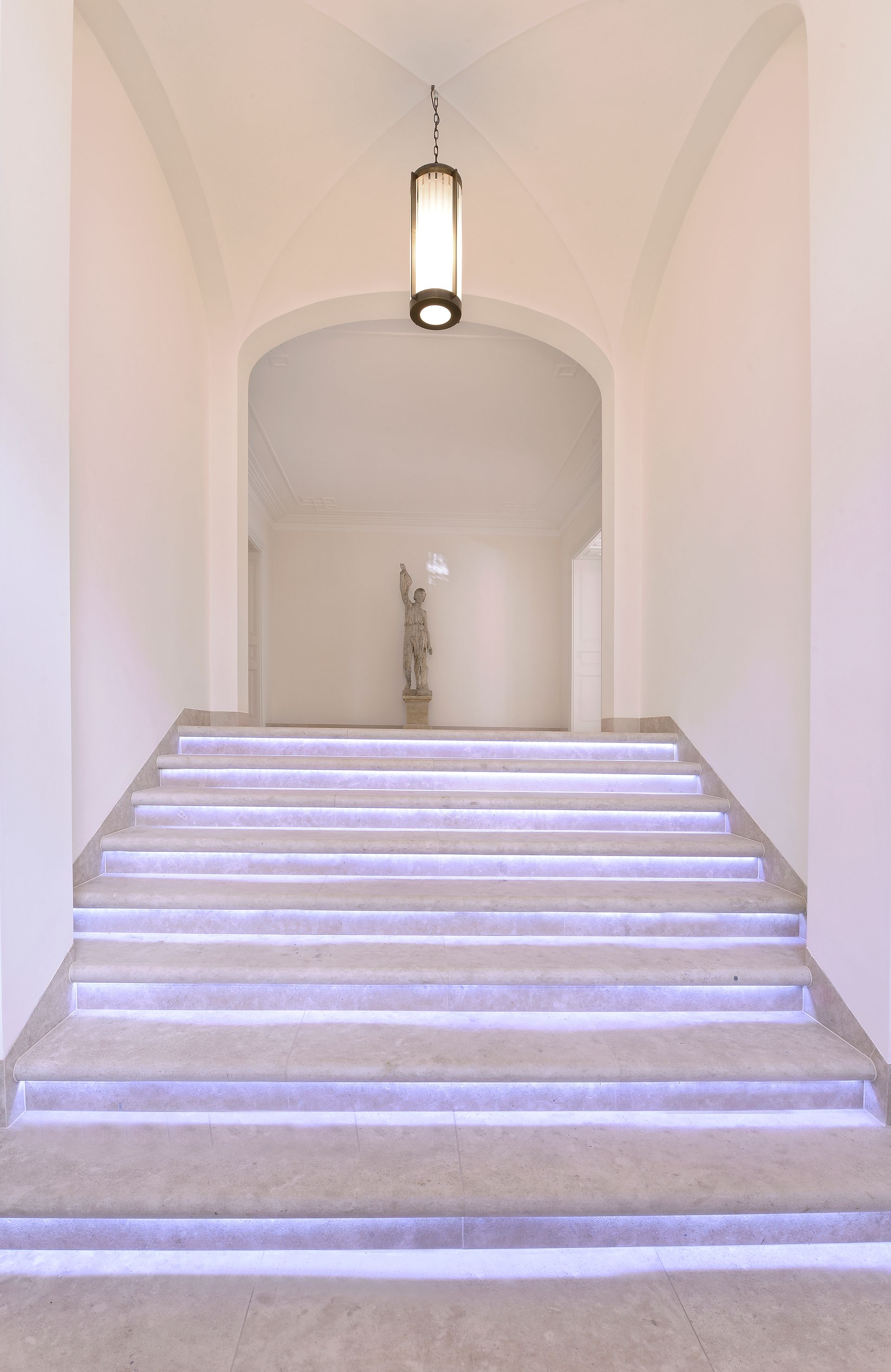 White staircase leading to an arched hallway with a hanging lantern.