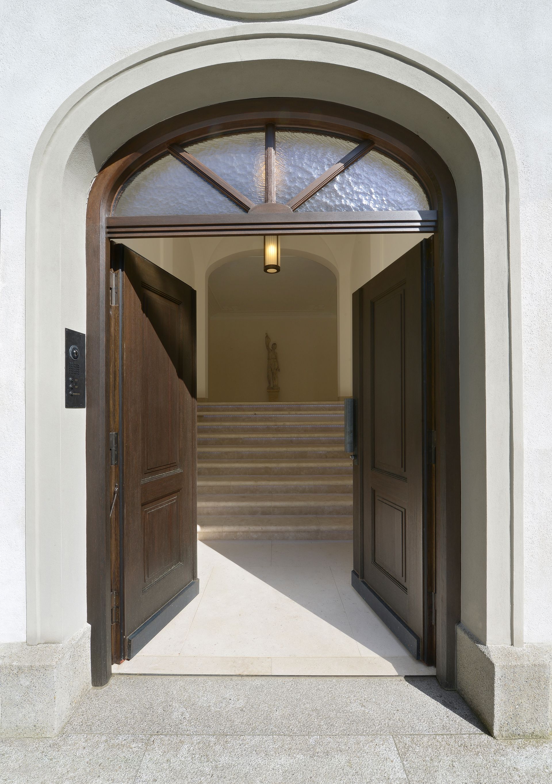 Open arched doorway with wooden double doors leading to a stairwell inside a white building.