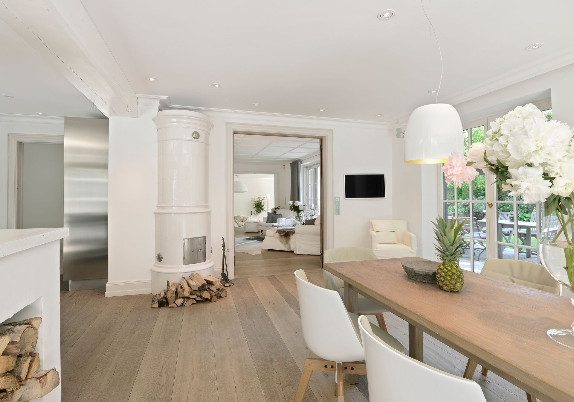 Bright modern dining room with white walls, wood floor, and a table set with flowers and white chairs