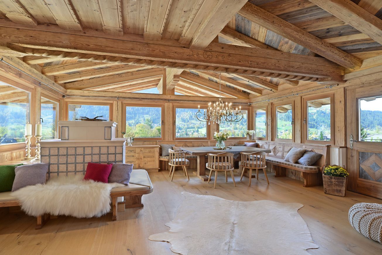 Rustic cabin living room with large windows, wooden beams, sofa, dining table, and mountain view