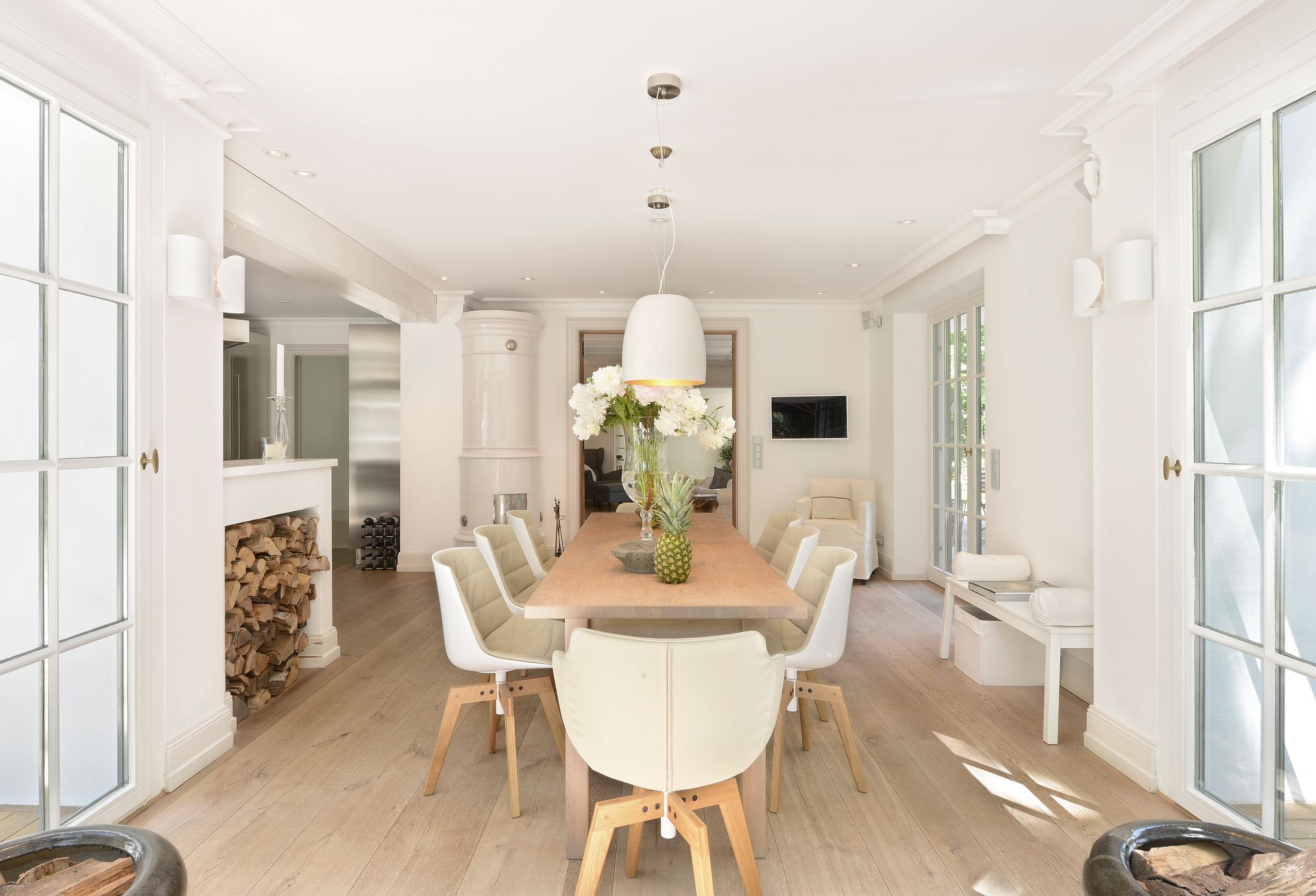 Bright dining room with long wooden table, white chairs, flowers, and French doors on both sides