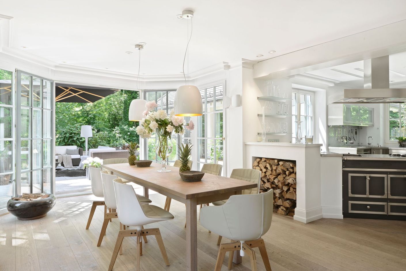 Bright, airy open kitchen and dining room with white walls, wood table, and large windows overlooking greenery.