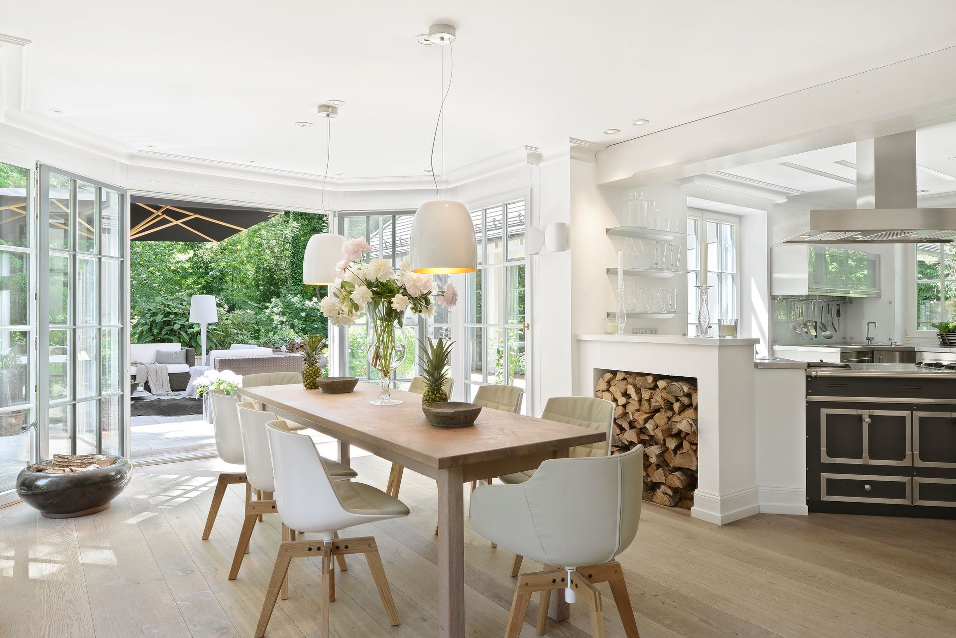 Bright open dining room and kitchen with white walls, wood table, and large windows overlooking greenery