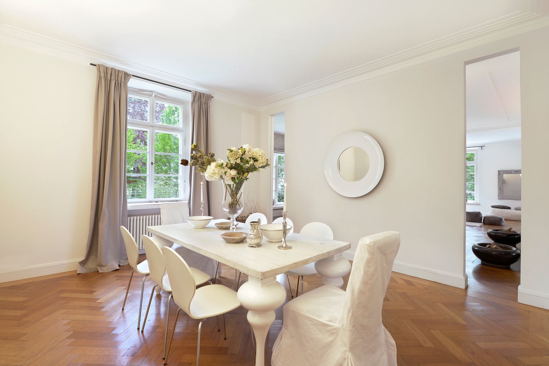 Bright dining room with white table, cream chairs, wooden floors, and flowers by a window