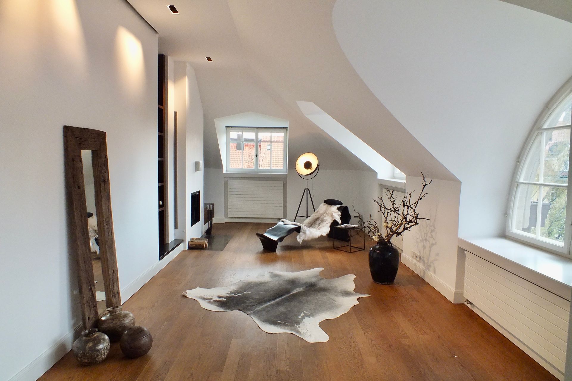 Bright attic living room with wood floor, cowhide rug, arched window, and modern lounge chair