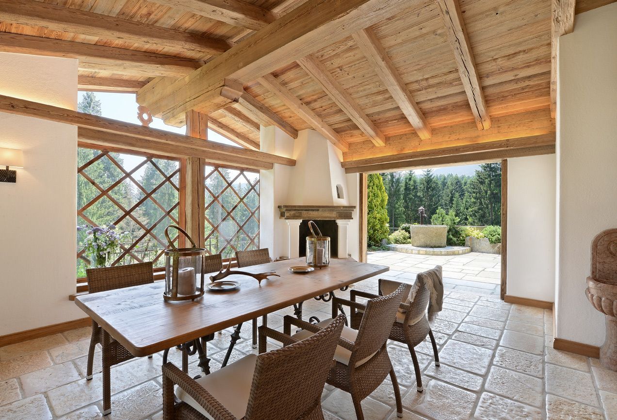 Bright rustic dining room with long wooden table, woven chairs, fireplace, and open view to a sunlit garden
