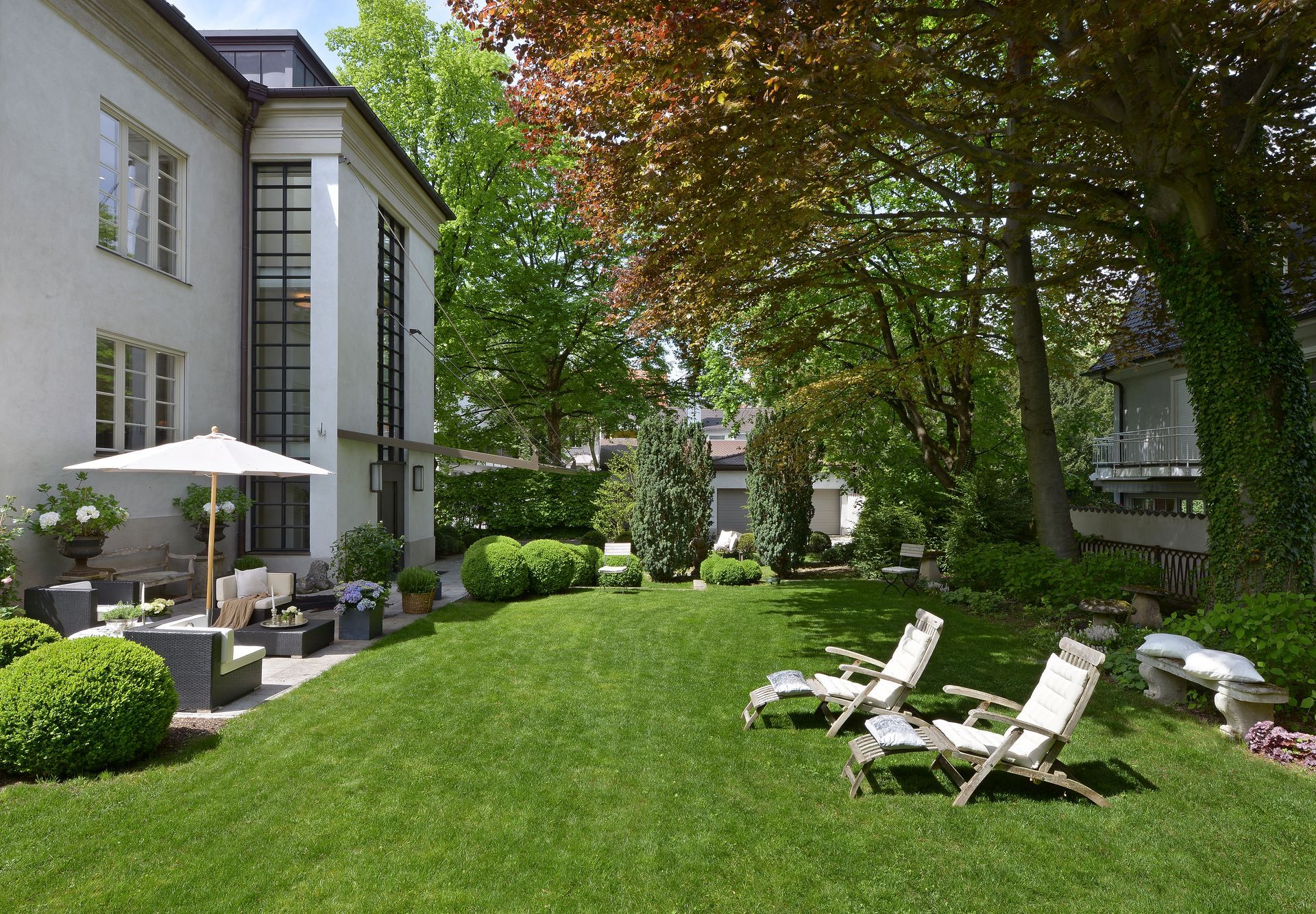 Sunny courtyard garden with lawn, lounge chairs, umbrellas, and apartment buildings.