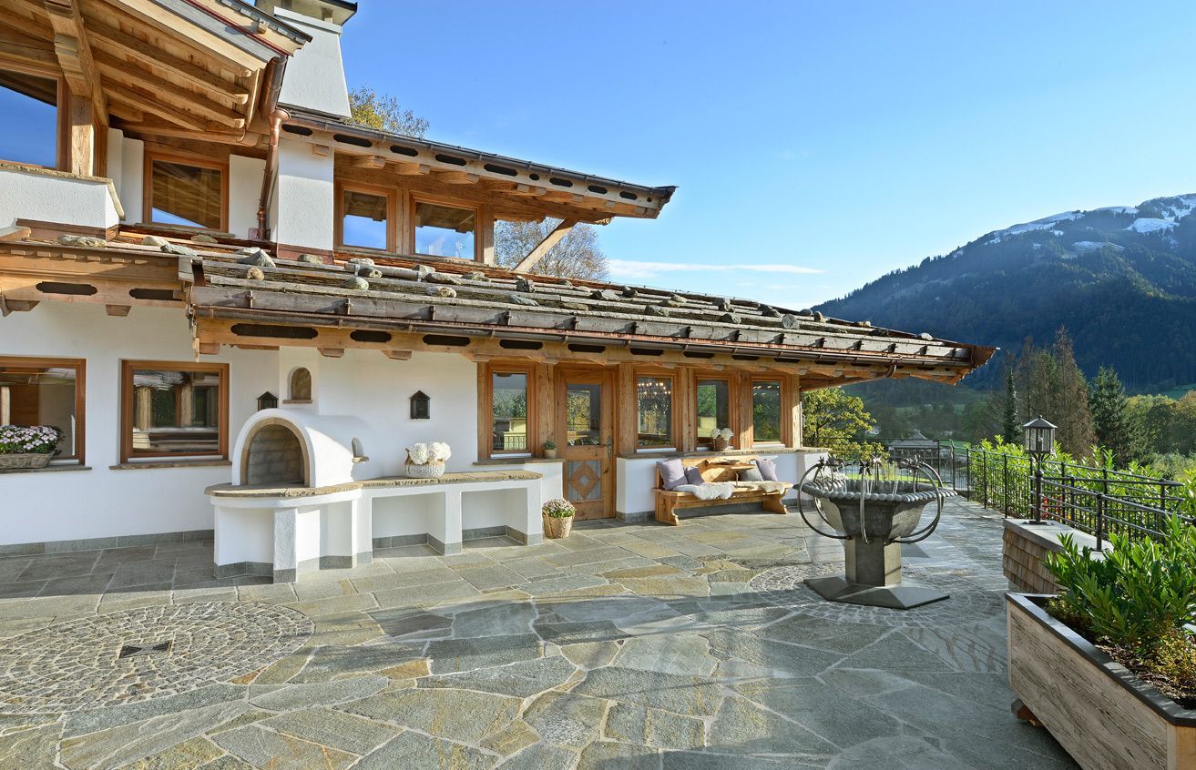 Stone patio beside a traditional alpine house with wooden balconies and mountain views under a clear sky