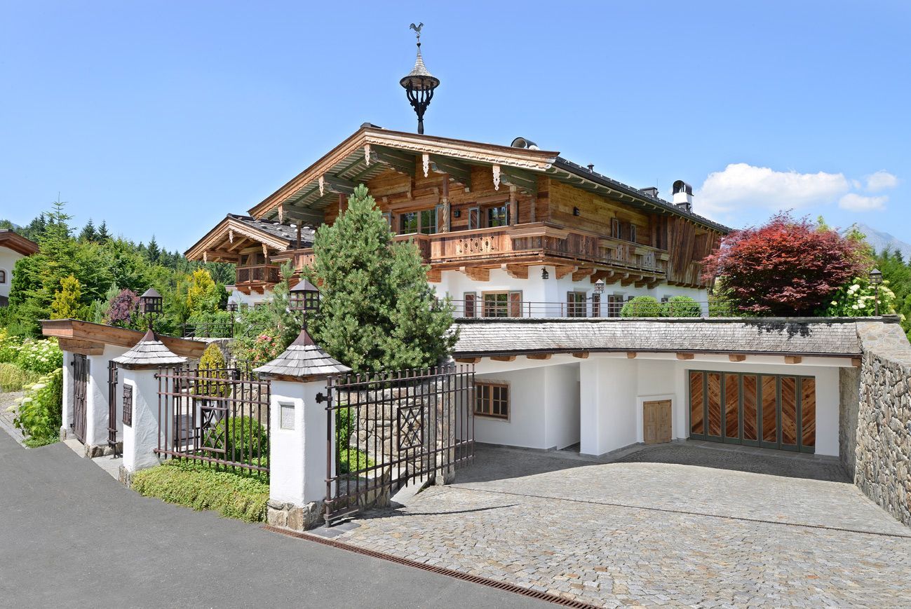 Chalet-style house with flower boxes, stone driveway, and mountain view under a blue sky