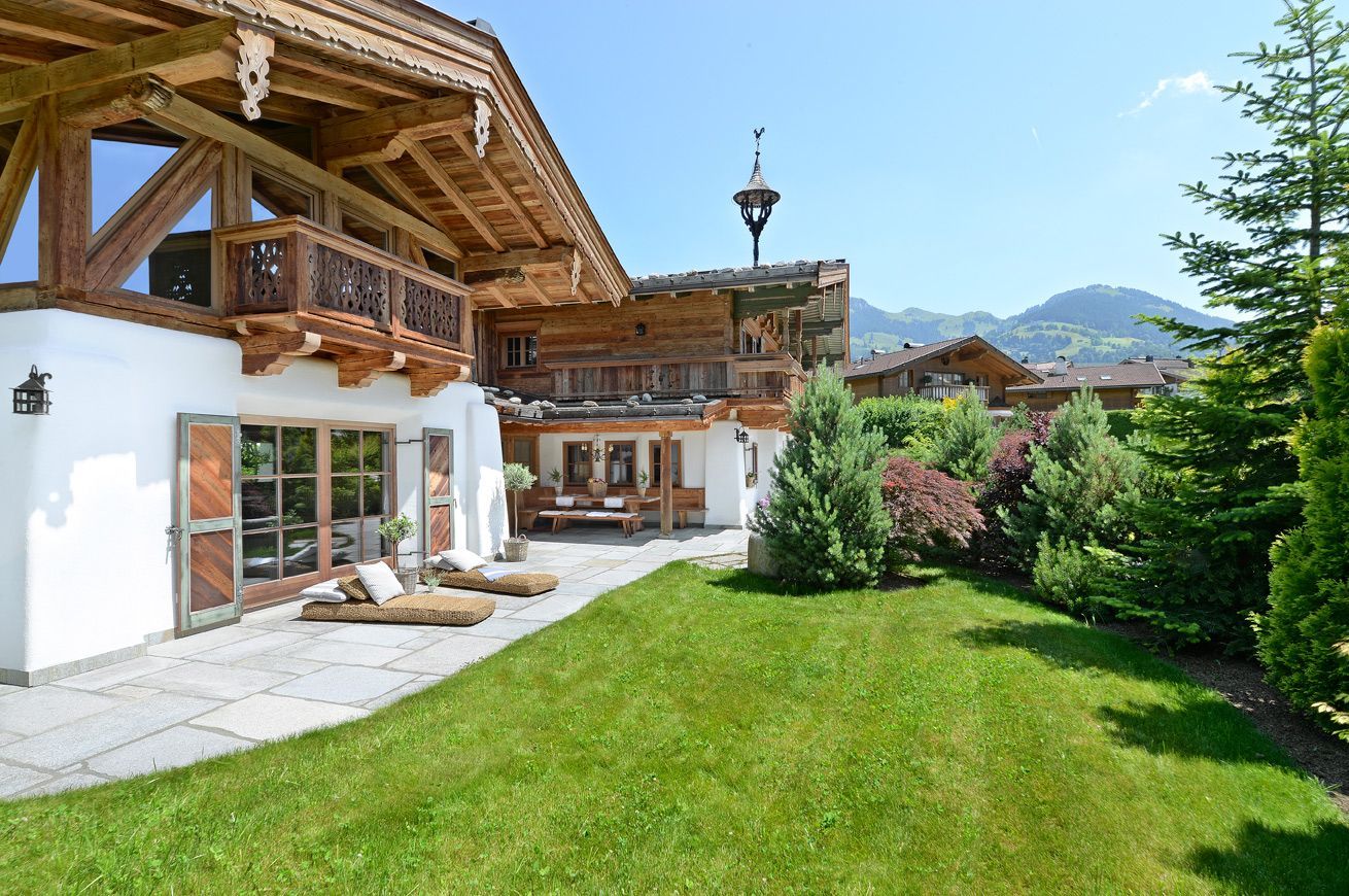 Chalet with wooden balconies and a green lawn in a sunny mountain garden