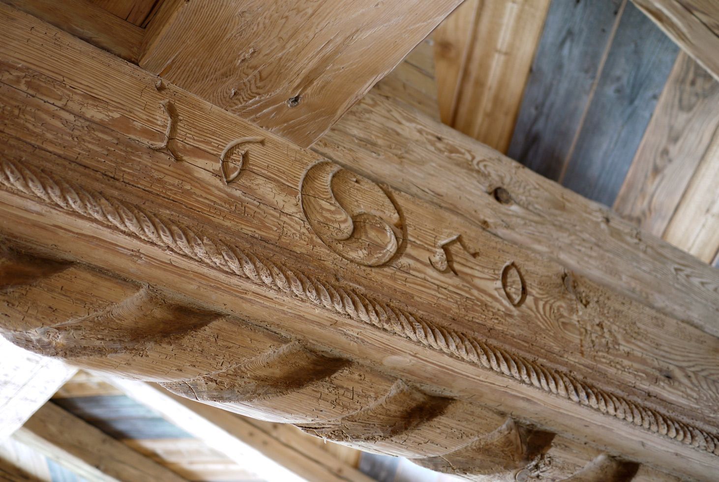 Close-up of carved wooden beam with decorative vine pattern under a rustic roof